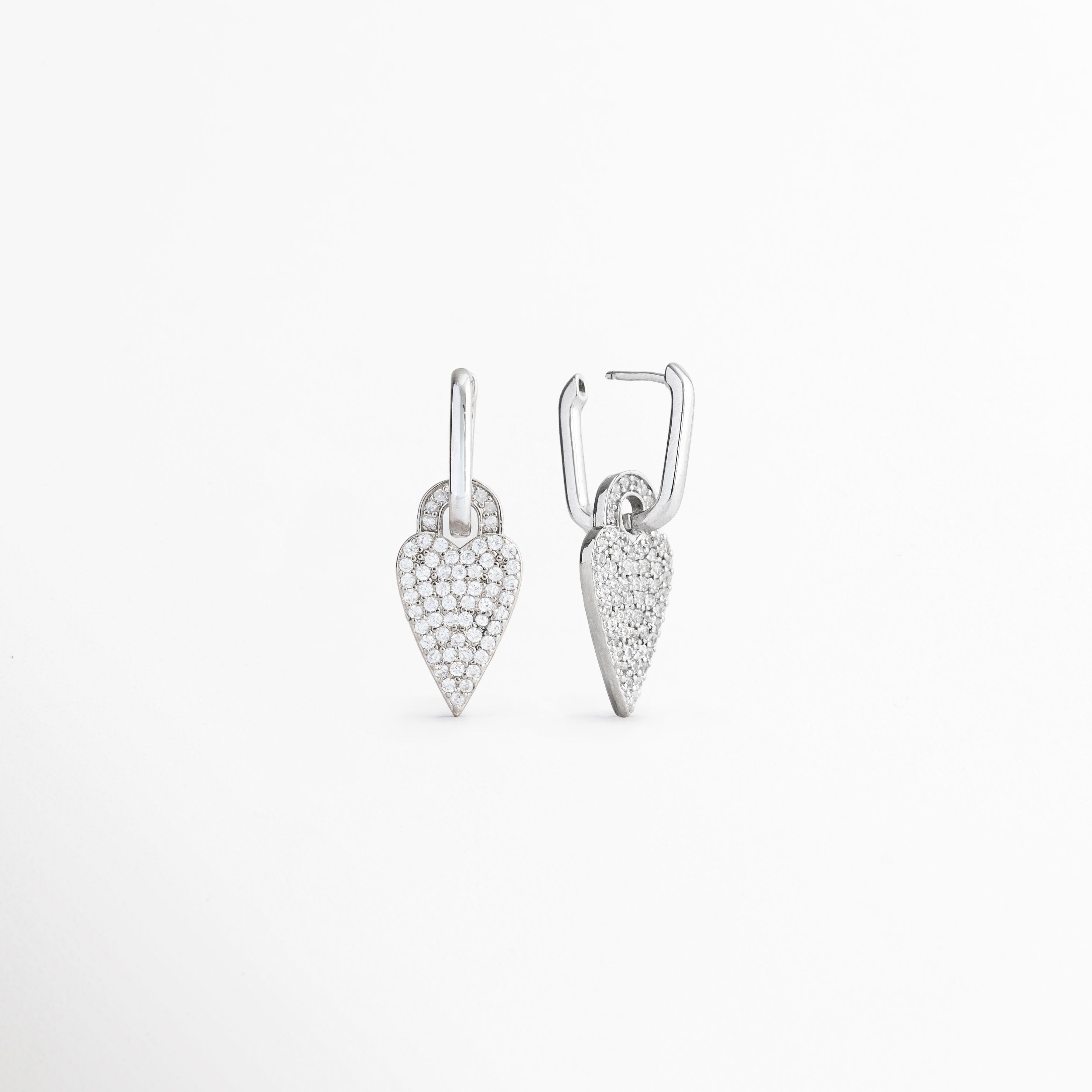 Vista inclinada de aretes Silver Velvet Hoops con zirconias, Pendientes con corazón brillante y diseño contemporáneo, Detalle de aretes plateados con charm femenino, Aretes tipo hoop con corazón y acabado elegante, Vista complementaria de pendientes con dije de zirconias.