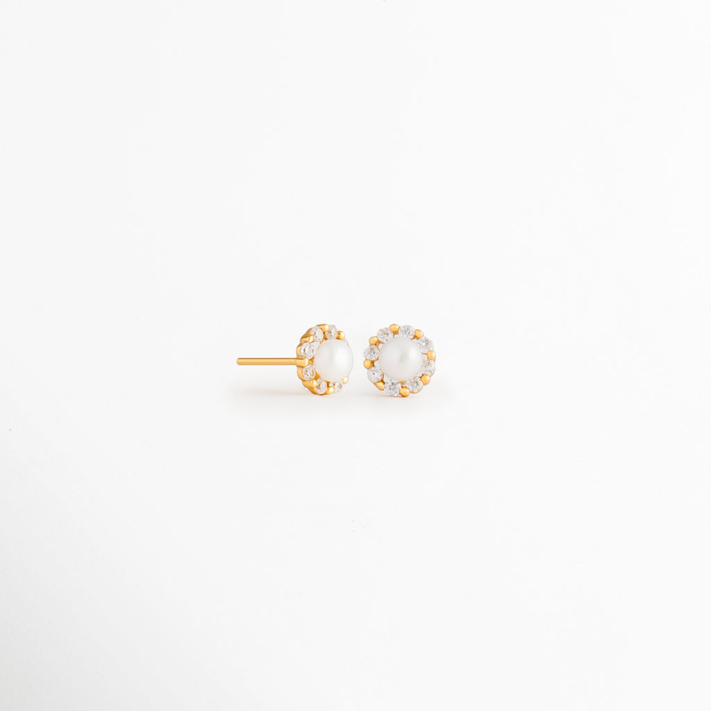 Vista en ángulo de los Aretes Zerina Golden Studs mostrando el perfil de la zirconia y el broche tipo poste, Perspectiva de los Aretes Zerina Golden Studs con acabado en Oro 14K y zirconia brillante, Aretes Zerina Golden Studs fotografiados de perfil resaltando el engaste de la zirconia, Vista diagonal de los Aretes Zerina Golden Studs elaborados en Plata de Ley 925 con recubrimiento en Oro 14K, Aretes Zerina Golden Studs en perspectiva mostrando su diseño delicado y elegante.