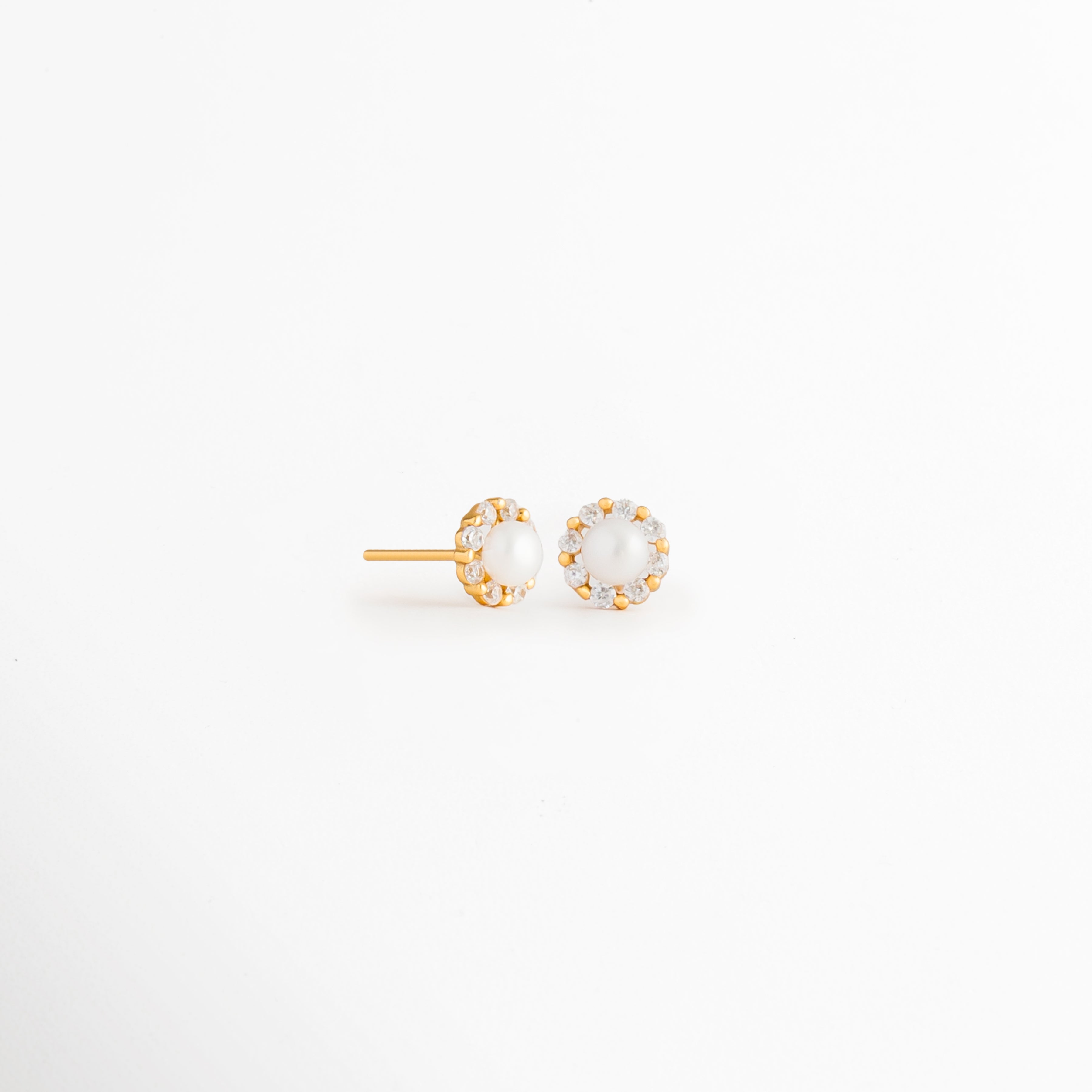 Vista en ángulo de los Aretes Zerina Golden Studs mostrando el perfil de la zirconia y el broche tipo poste, Perspectiva de los Aretes Zerina Golden Studs con acabado en Oro 14K y zirconia brillante, Aretes Zerina Golden Studs fotografiados de perfil resaltando el engaste de la zirconia, Vista diagonal de los Aretes Zerina Golden Studs elaborados en Plata de Ley 925 con recubrimiento en Oro 14K, Aretes Zerina Golden Studs en perspectiva mostrando su diseño delicado y elegante.