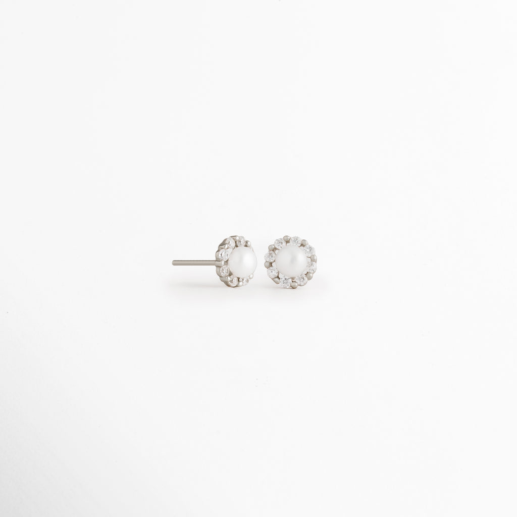 Vista en ángulo de los Aretes Zerina Silver Studs mostrando el perfil de la zirconia y el broche tipo poste, Perspectiva de los Aretes Zerina Silver Studs con acabado en Oro Blanco 14K y zirconia brillante, Aretes Zerina Silver Studs fotografiados de perfil resaltando el engaste de la zirconia, Vista diagonal de los Aretes Zerina Silver Studs elaborados en Plata de Ley 925 con recubrimiento en Oro Blanco 14K, Aretes Zerina Silver Studs en perspectiva mostrando su diseño delicado y sofisticado.