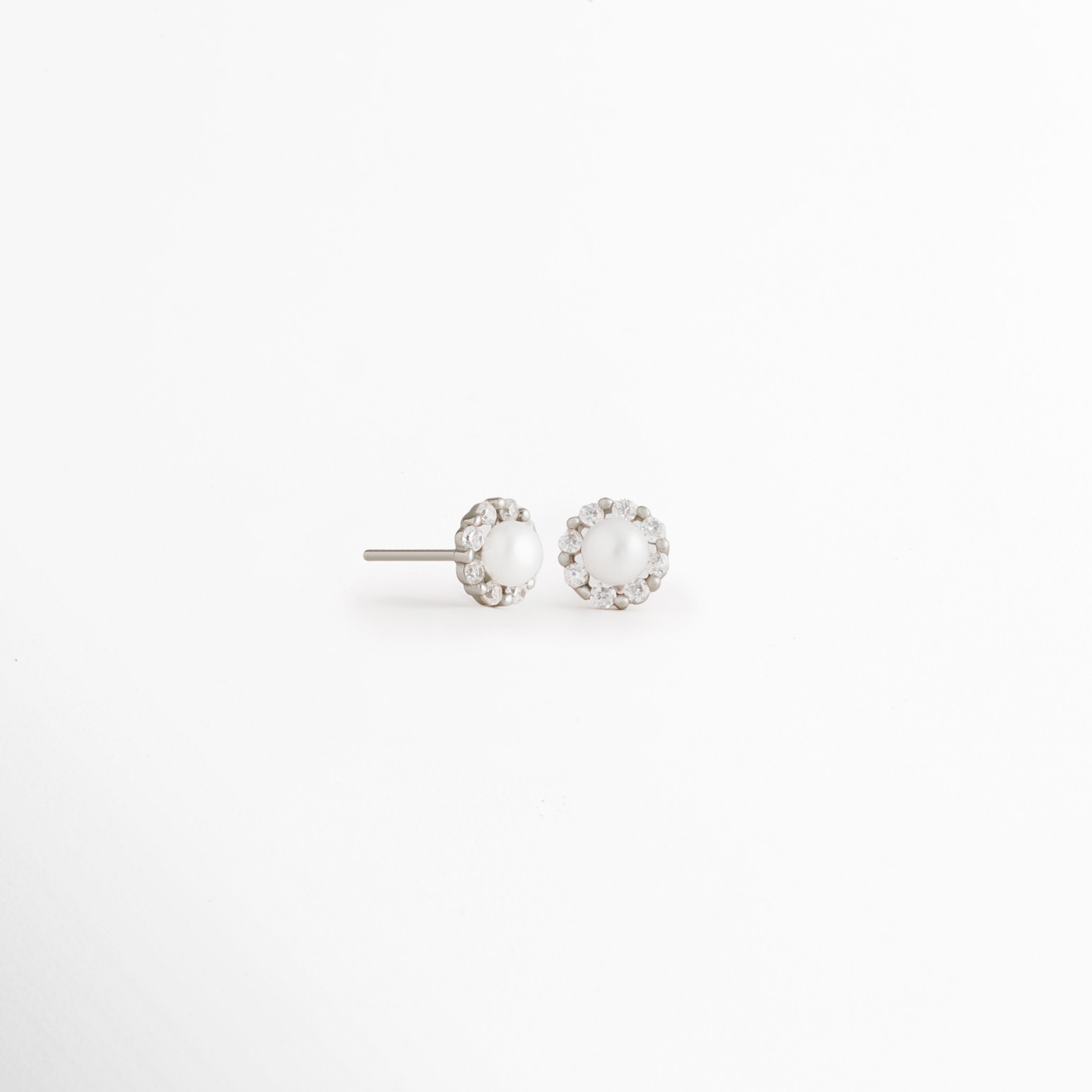 Vista en ángulo de los Aretes Zerina Silver Studs mostrando el perfil de la zirconia y el broche tipo poste, Perspectiva de los Aretes Zerina Silver Studs con acabado en Oro Blanco 14K y zirconia brillante, Aretes Zerina Silver Studs fotografiados de perfil resaltando el engaste de la zirconia, Vista diagonal de los Aretes Zerina Silver Studs elaborados en Plata de Ley 925 con recubrimiento en Oro Blanco 14K, Aretes Zerina Silver Studs en perspectiva mostrando su diseño delicado y sofisticado.