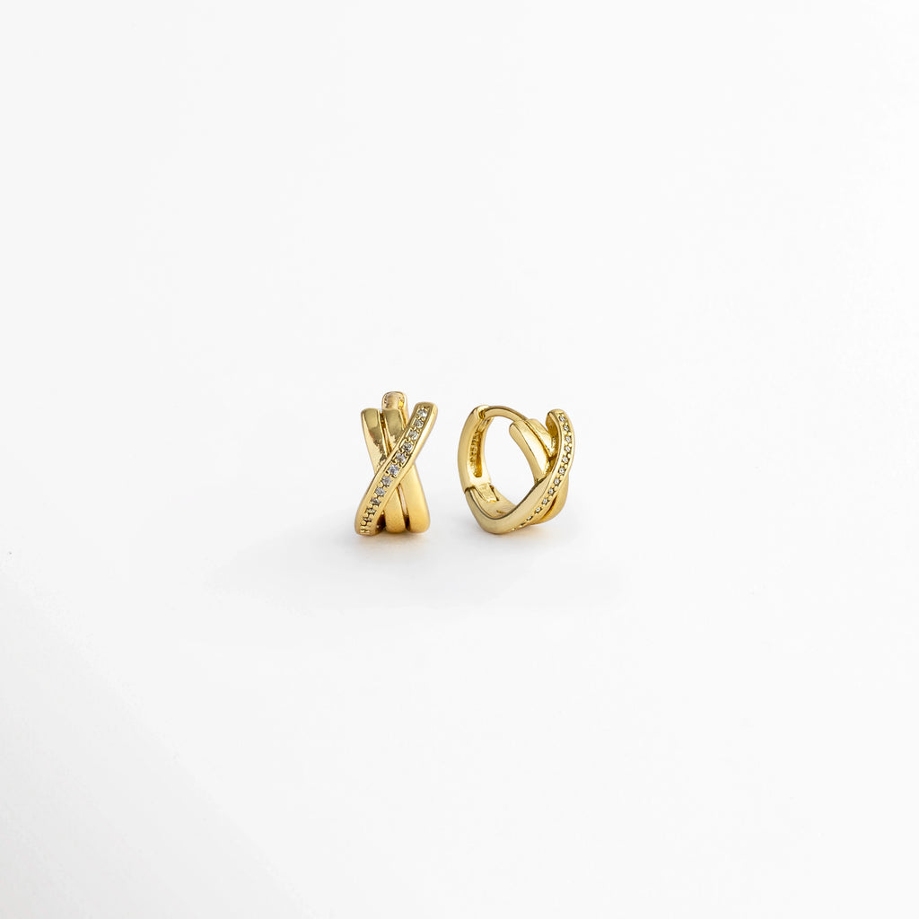 Vista en ángulo y perfil de los Diana Golden Hoops mostrando el grosor de 0.6 cm y el broche de bisagra articulada, Acercamiento a la silueta circular compacta del huggie dorado entrelazado con banda de circonias, Muestra en tres cuartos del relieve tridimensional de los tres aros cruzados enchapados en oro, Vista lateral del mecanismo de cierre huggie integrado en los aretes dorados de 1.1 cm.