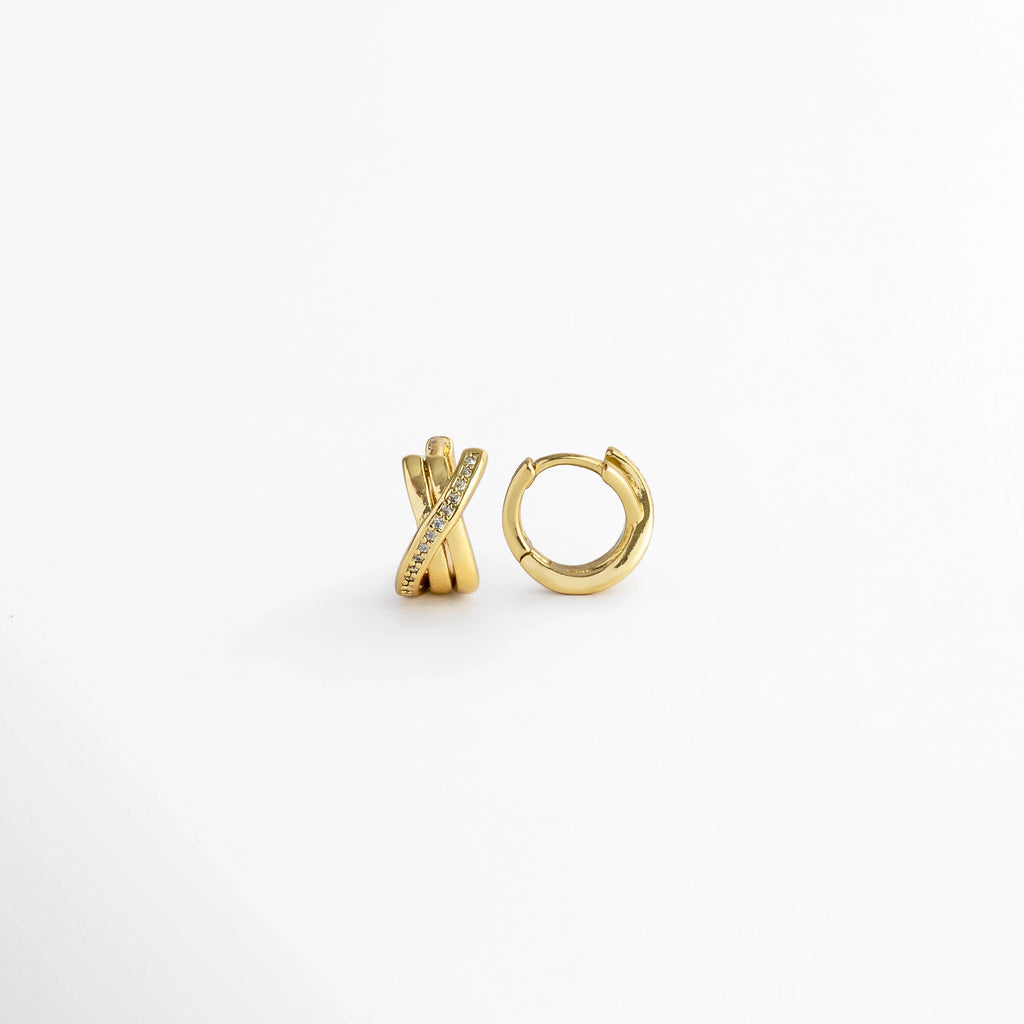 Vista lateral de los Diana Golden Hoops cerrados mostrando la bisagra posterior y el ajuste de poste continuo, Detalle del cierre tipo click/snap en el perfil arqueado de los aros dorados entrelazados de 1.1 cm, Muestra de perfil del grosor de 0.6 cm y las tres bandas doradas superpuestas con circonias, Acercamiento lateral al acabado enchapado en oro de alta precisión en la estructura del huggie.