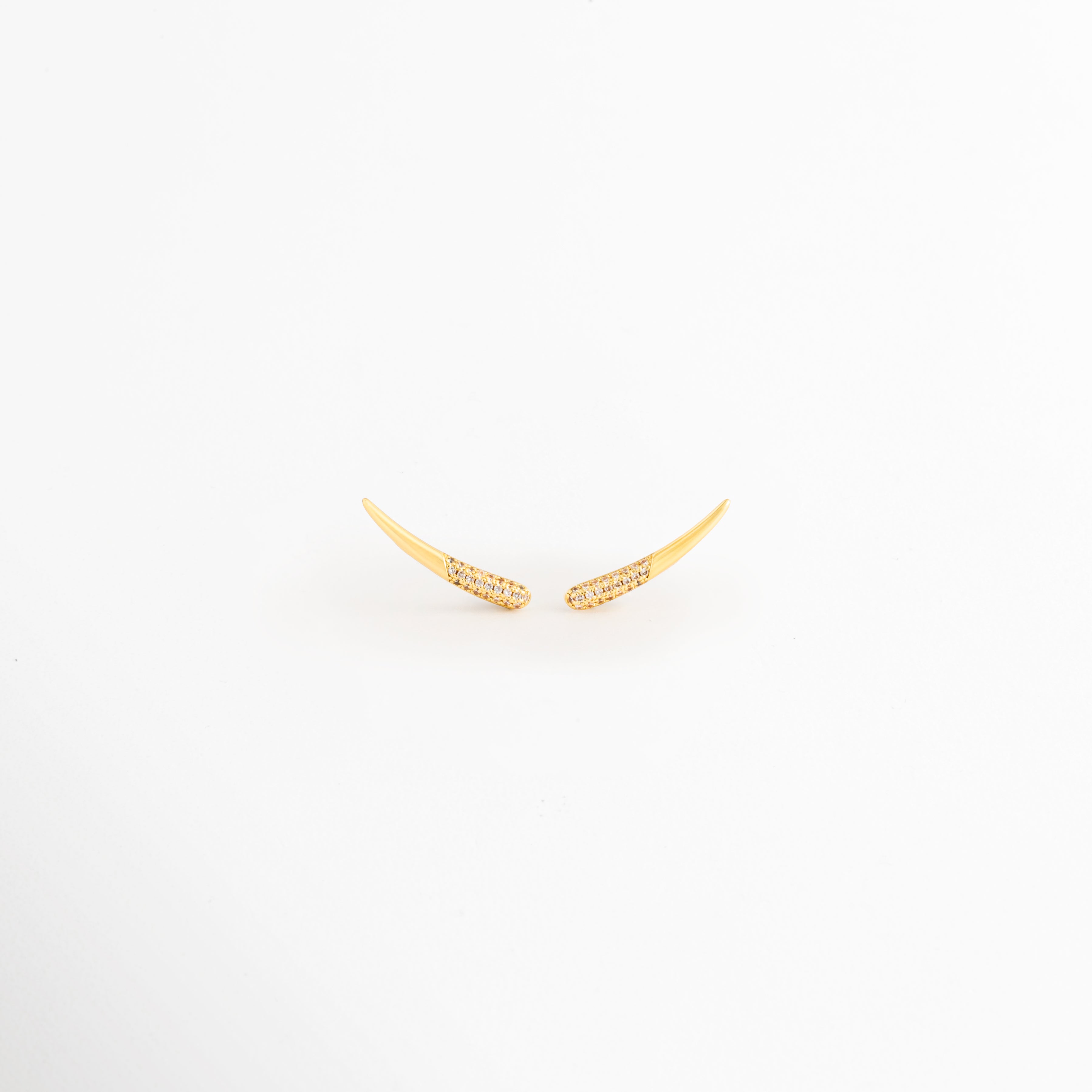 Aretes Golden Zerald de cobre con recubrimiento en Oro e incrustaciones de zirconias sobre fondo blanco, Vista frontal de los Aretes Golden Zerald con diseño curvo y zirconias brillantes, Aretes Golden Zerald con diseño minimalista curvo y acabado en Oro, Par de Aretes Golden Zerald con zirconias incrustadas y acabado dorado brillante, Aretes Golden Zerald con diseño elegante de líneas curvas y zirconias.