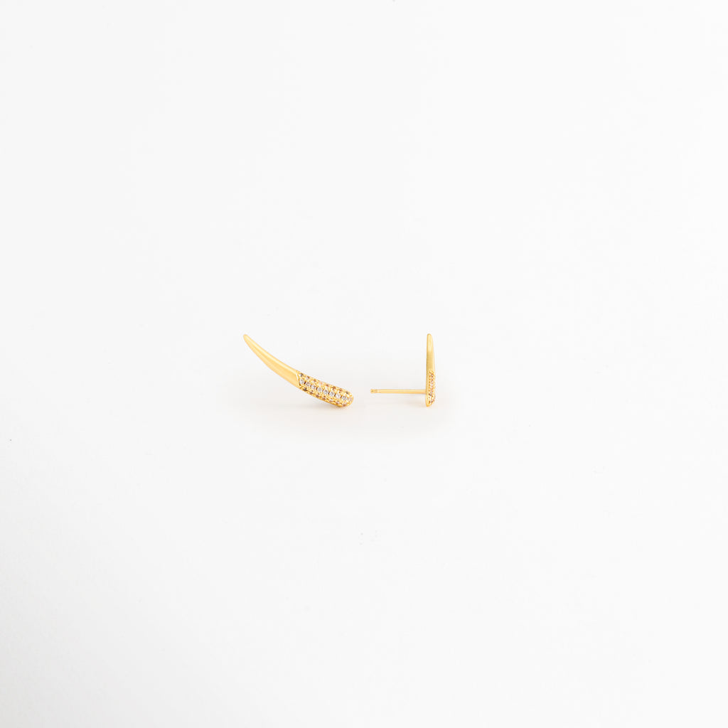 Vista en ángulo de los Aretes Golden Zerald mostrando el perfil curvo y las zirconias, Perspectiva de los Aretes Golden Zerald con acabado en Oro y diseño estilizado, Aretes Golden Zerald fotografiados de perfil resaltando el brillo de las zirconias, Vista diagonal de los Aretes Golden Zerald elaborados en cobre con recubrimiento en Oro, Aretes Golden Zerald en perspectiva mostrando su diseño delicado y contemporáneo.