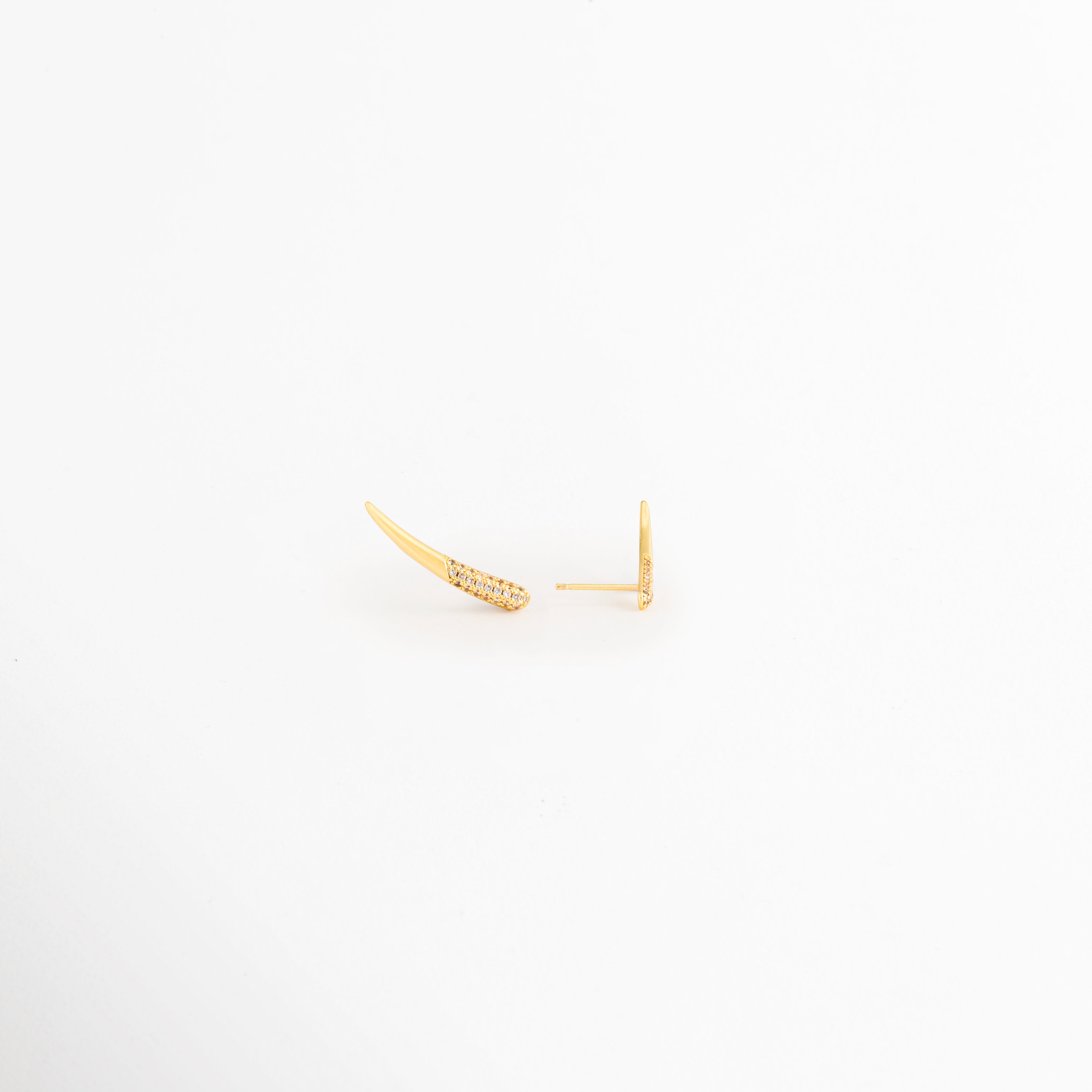 Vista en ángulo de los Aretes Golden Zerald mostrando el perfil curvo y las zirconias, Perspectiva de los Aretes Golden Zerald con acabado en Oro y diseño estilizado, Aretes Golden Zerald fotografiados de perfil resaltando el brillo de las zirconias, Vista diagonal de los Aretes Golden Zerald elaborados en cobre con recubrimiento en Oro, Aretes Golden Zerald en perspectiva mostrando su diseño delicado y contemporáneo.