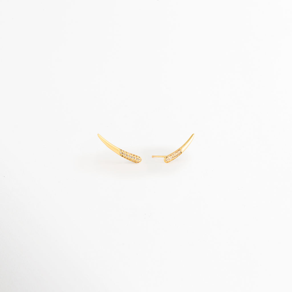Vista lateral de los Aretes Golden Zerald mostrando el broche tipo poste y el perfil curvo, Perfil de los Aretes Golden Zerald con acabado en Oro y zirconias incrustadas, Aretes Golden Zerald en vista lateral destacando el sistema de cierre y su diseño elegante, Detalle lateral de los Aretes Golden Zerald elaborados en cobre con acabado dorado brillante, Vista de costado de los Aretes Golden Zerald con diseño curvo y zirconias.