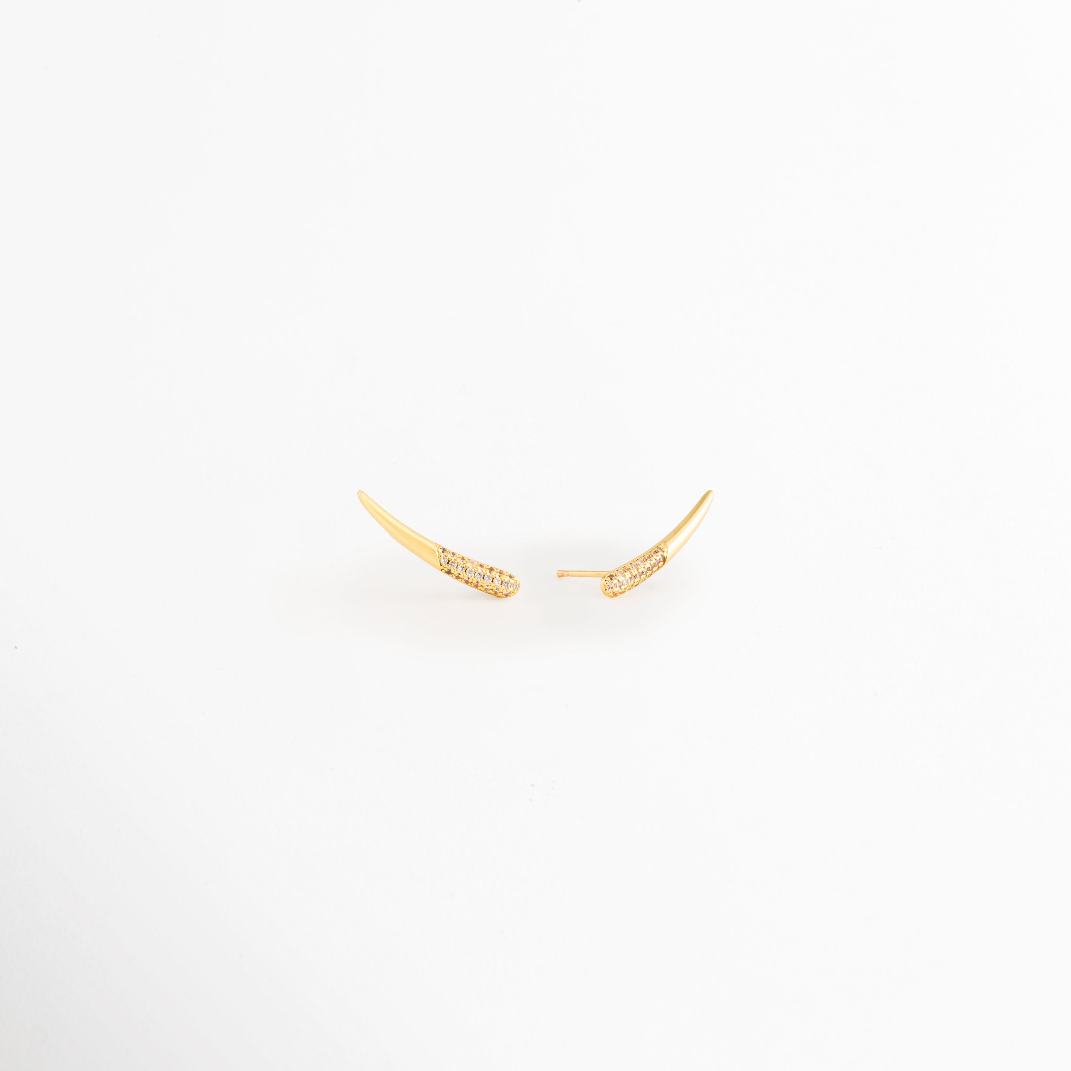 Vista lateral de los Aretes Golden Zerald mostrando el broche tipo poste y el perfil curvo, Perfil de los Aretes Golden Zerald con acabado en Oro y zirconias incrustadas, Aretes Golden Zerald en vista lateral destacando el sistema de cierre y su diseño elegante, Detalle lateral de los Aretes Golden Zerald elaborados en cobre con acabado dorado brillante, Vista de costado de los Aretes Golden Zerald con diseño curvo y zirconias.
