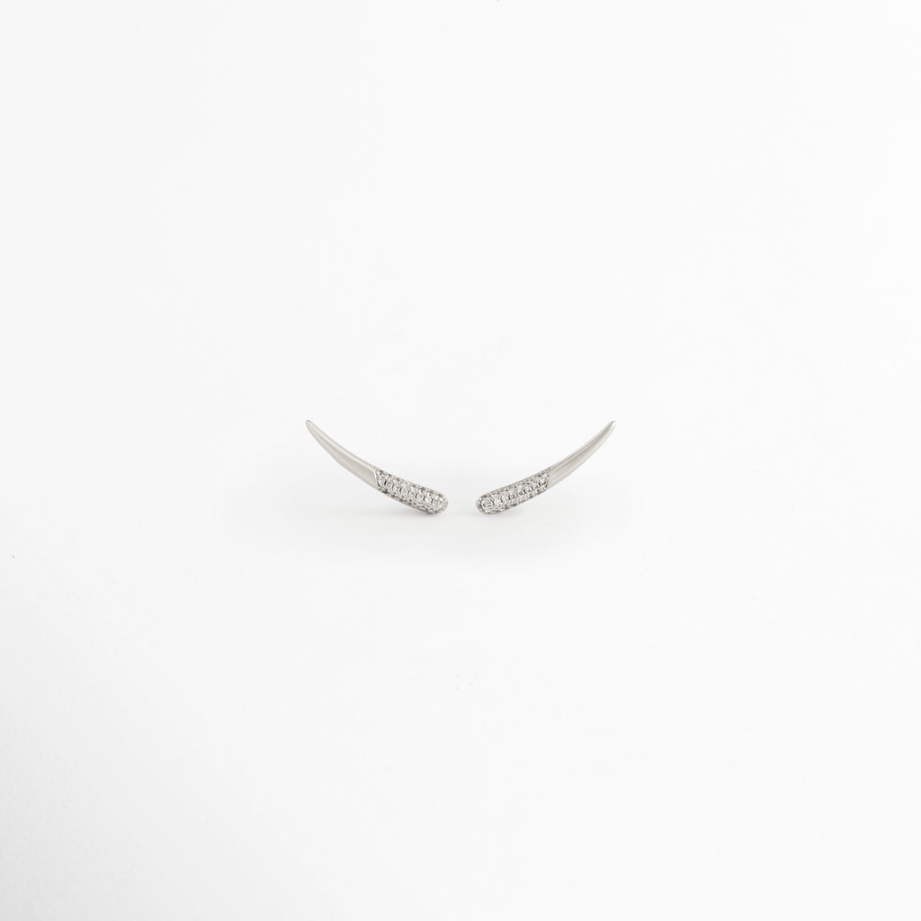 Aretes Silver Zerald de cobre con recubrimiento en Oro Blanco e incrustaciones de zirconias sobre fondo blanco, Vista frontal de los Aretes Silver Zerald con diseño curvo y zirconias brillantes, Aretes Silver Zerald con diseño minimalista curvo y acabado en Oro Blanco, Par de Aretes Silver Zerald con zirconias incrustadas y acabado plateado brillante, Aretes Silver Zerald con diseño elegante de líneas curvas y zirconias.