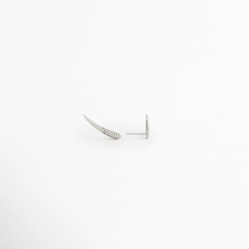 Vista en ángulo de los Aretes Silver Zerald mostrando el perfil curvo y las zirconias, Perspectiva de los Aretes Silver Zerald con acabado en Oro Blanco y diseño estilizado, Aretes Silver Zerald fotografiados de perfil resaltando el brillo de las zirconias, Vista diagonal de los Aretes Silver Zerald elaborados en cobre con recubrimiento en Oro Blanco, Aretes Silver Zerald en perspectiva mostrando su diseño delicado y contemporáneo.