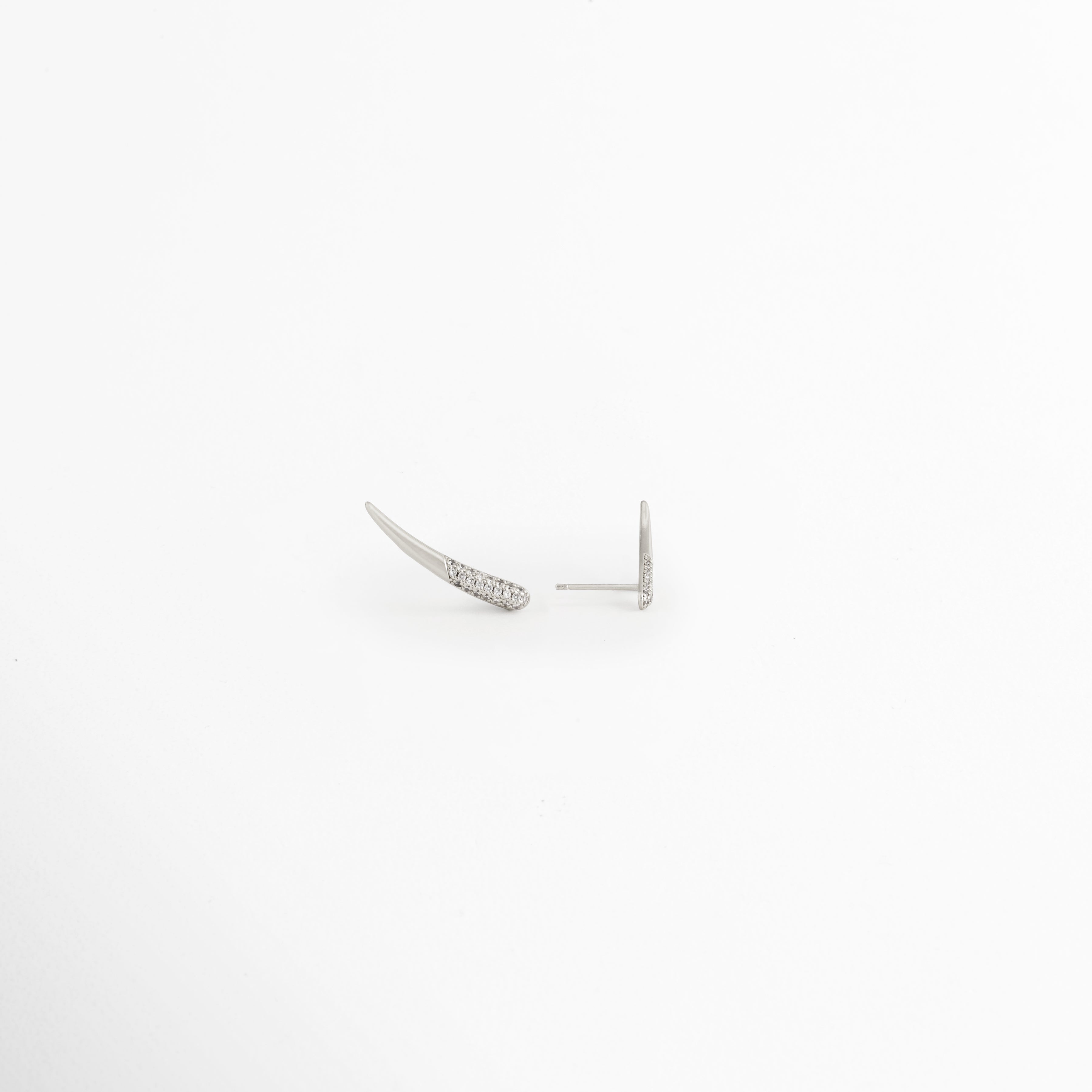 Vista en ángulo de los Aretes Silver Zerald mostrando el perfil curvo y las zirconias, Perspectiva de los Aretes Silver Zerald con acabado en Oro Blanco y diseño estilizado, Aretes Silver Zerald fotografiados de perfil resaltando el brillo de las zirconias, Vista diagonal de los Aretes Silver Zerald elaborados en cobre con recubrimiento en Oro Blanco, Aretes Silver Zerald en perspectiva mostrando su diseño delicado y contemporáneo.