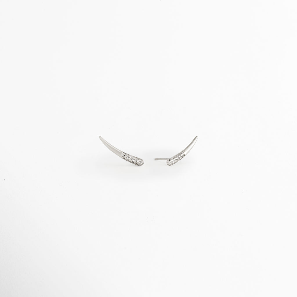 Vista lateral de los Aretes Silver Zerald mostrando el broche tipo poste y el perfil curvo, Perfil de los Aretes Silver Zerald con acabado en Oro Blanco y zirconias incrustadas, Aretes Silver Zerald en vista lateral destacando el sistema de cierre y su diseño elegante, Detalle lateral de los Aretes Silver Zerald elaborados en cobre con acabado plateado brillante, Vista de costado de los Aretes Silver Zerald con diseño curvo y zirconias.