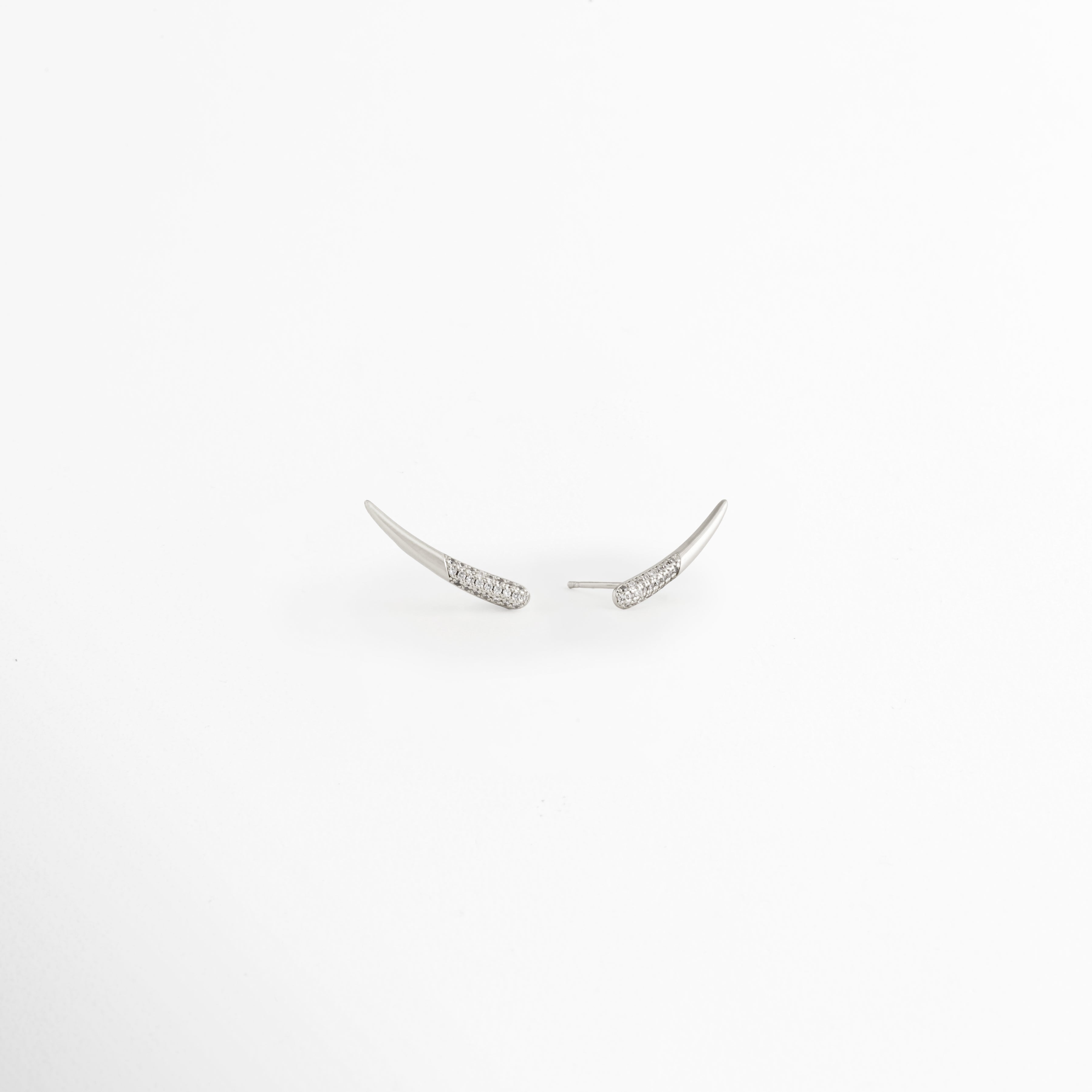 Vista lateral de los Aretes Silver Zerald mostrando el broche tipo poste y el perfil curvo, Perfil de los Aretes Silver Zerald con acabado en Oro Blanco y zirconias incrustadas, Aretes Silver Zerald en vista lateral destacando el sistema de cierre y su diseño elegante, Detalle lateral de los Aretes Silver Zerald elaborados en cobre con acabado plateado brillante, Vista de costado de los Aretes Silver Zerald con diseño curvo y zirconias.