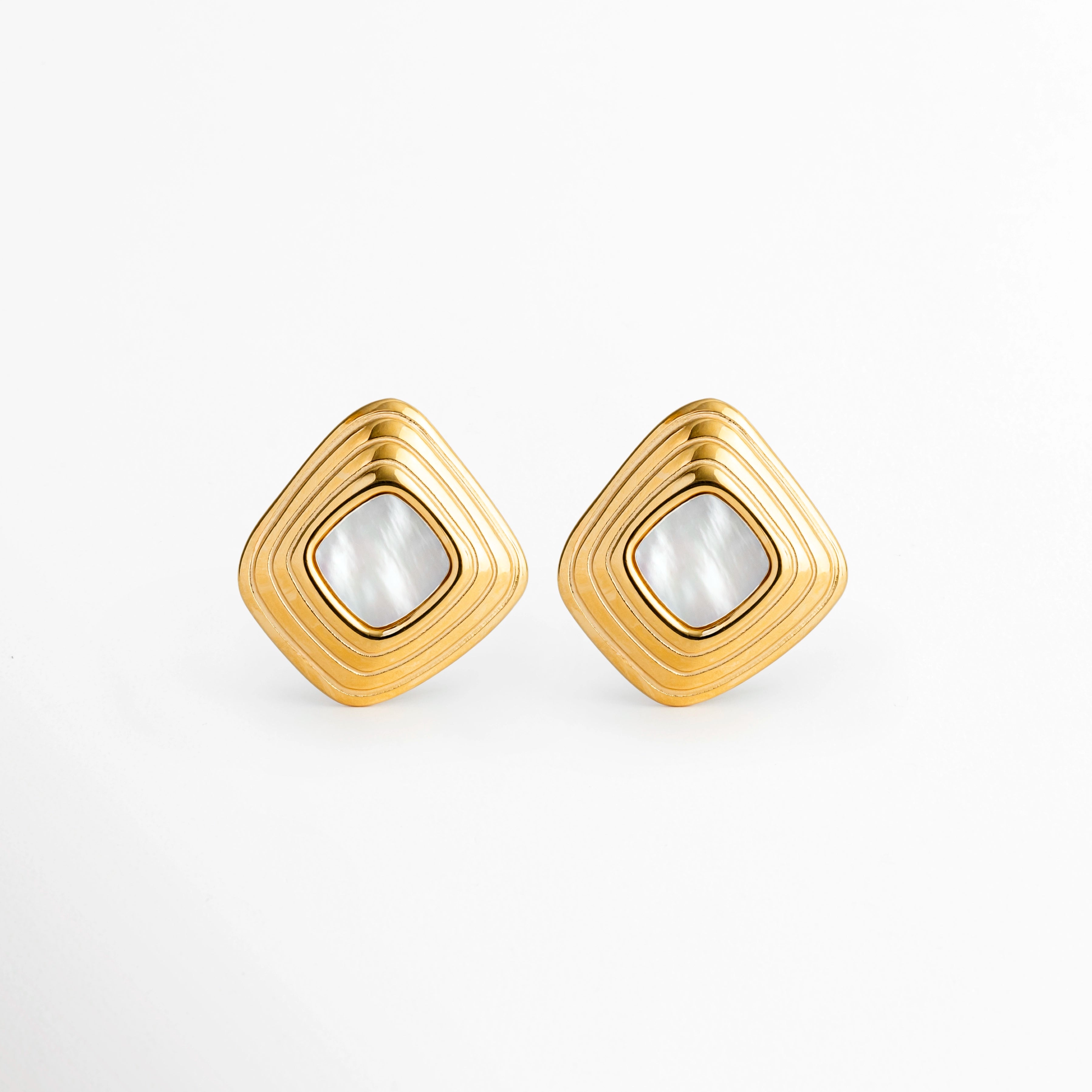 Aretes Lara White Studs en forma de rombo dorado con textura de relieve acanalado y centro de piedra blanca nacarada, vista frontal sobre fondo blanco, Par de topos geométricos de 2.2 x 2.1 cm enchapados en oro 18K con bisel acanalado y gema central de tono blanco madreperla, Vista de frente de aretes vintage de acero inoxidable dorados con forma de diamante o rombo e inserción de piedra blanca, Aretes estilo stud retro de marco acanalado en oro cálido con incrustación