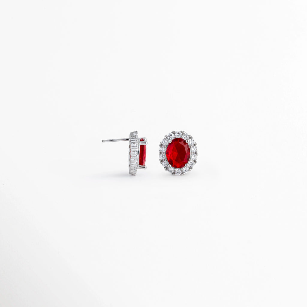Vista lateral de los aretes Crimson Studs mostrando el poste de Plata Ley 925 para oreja perforada, Acercamiento de perfil a la estructura del broquel platinado y la altura del engaste de la gema carmesí, Detalle del sistema de ajuste por poste posterior y mariposa de los studs con pedrería roja, Muestra de la confección en plata ley 925 con recubrimiento platinado de alta durabilidad.