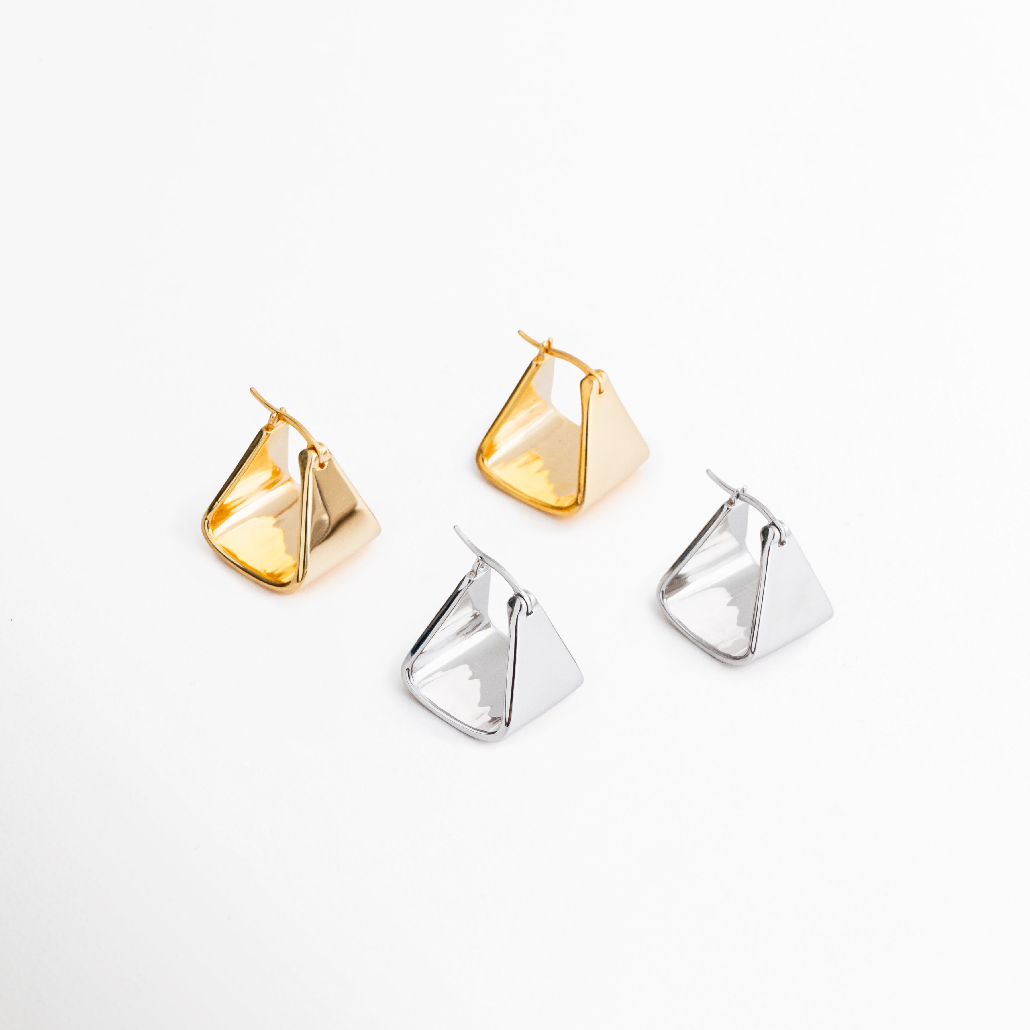 Aretes Corot disponibles en acabado dorado y oro blanco 18K con diseño triangular minimalista, Comparativa de colores de los aretes Corot en versiones dorada y plateada para diferentes estilos, Pendientes Corot geométricos en acabados metálicos brillantes, ideales para combinar con cualquier outfit, Colección de aretes Corot en tonos dorado y plata con diseño contemporáneo y versátil, Variantes de color de los aretes Corot con acabado premium y estilo minimalista.