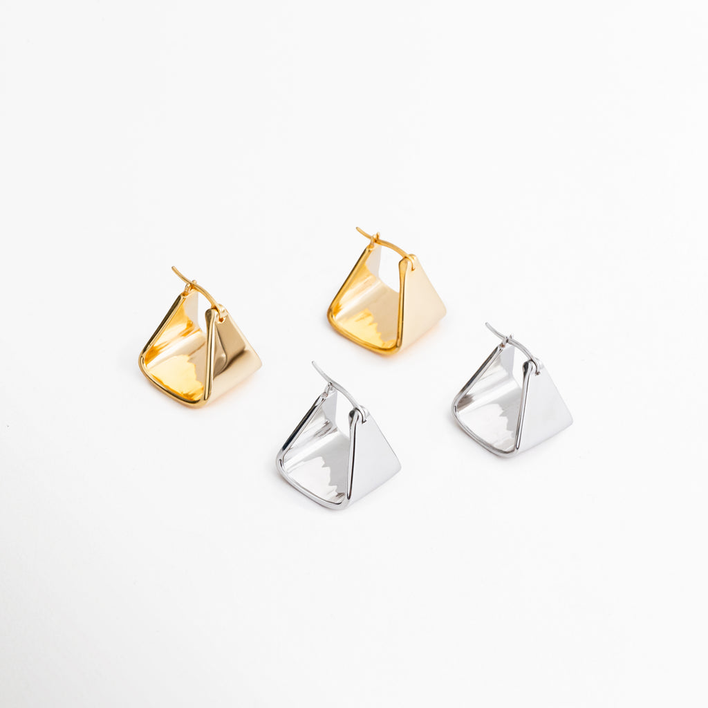 Aretes Corot disponibles en acabado oro blanco 18K y tono dorado, diseño triangular minimalista, Comparativa de colores de los aretes Corot en versiones plateada y dorada para diferentes estilos, Pendientes Corot con diseño geométrico triangular en acabados metálicos elegantes y versátiles, Colección de aretes Corot en tonos dorado y plata, ideales para complementar cualquier outfit, Variantes de color de los aretes minimalistas Corot con acabado brillante y estilo contemporáneo.