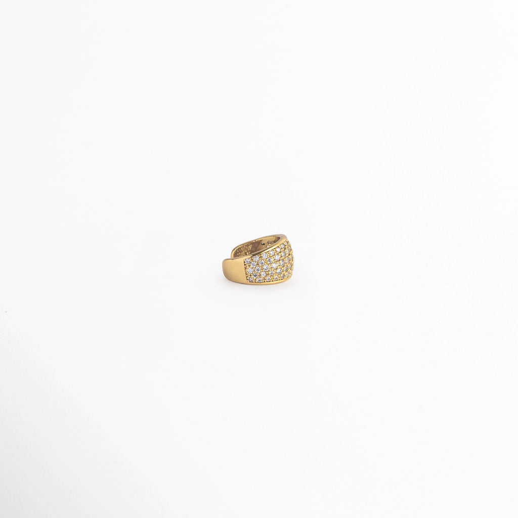 Vista en tres cuartos del Elara Golden Ear Cuff mostrando la curvatura abierta para ajuste a presión sobre el cartílago,  Acercamiento lateral al earcuff dorado de 1.2 cm de longitud con incrustaciones continuas de micro-circonias, Toma en ángulo que resalta el grosor abombado y los destellos de luz sobre la superficie de pedrería, Muestra de la silueta ergonómica del arete de presión enchapado en oro para oreja no perforada.