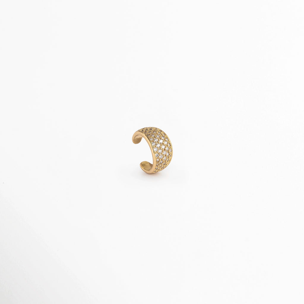 Vista lateral de perfil del Elara Golden Ear Cuff en posición vertical destacando el pulido dorado del interior y el reverso, Acercamiento al contorno curvo del earcuff de cartílago con frente de micro-circonias transparentes, Toma en ángulo que resalta el contraste entre la pedrería brillante y los bordes metálicos enchapados en oro, Muestra de la flexibilidad y firmeza de la pieza de 1.2 cm de largo para un ajuste seguro en la oreja
