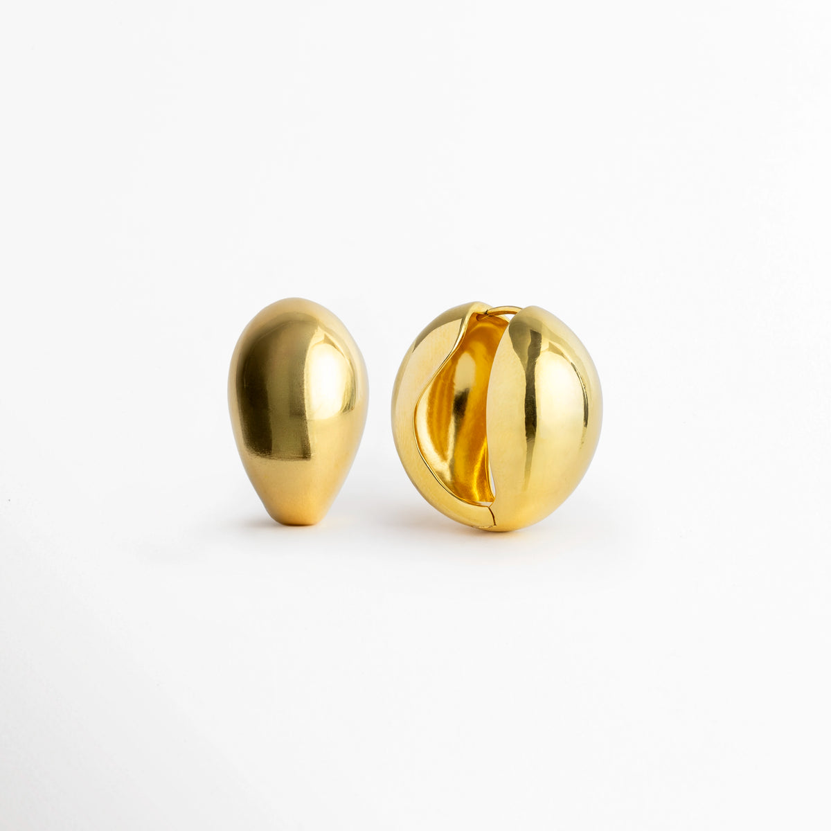 Aretes Golden Nevara vistos de frente y perfil mostrando la silueta de gota de agua y la apertura central de bisagra, Vista en ángulo de arete abombado dorado con diseño cóncavo posterior y cierre articulado, Acercamiento a la silueta orgánica y al reverso hueco de los aretes en forma de gota dorada, Detalle del volumen abultado de 1.8 cm de ancho del arete enchapado en oro sobre superficie clara.