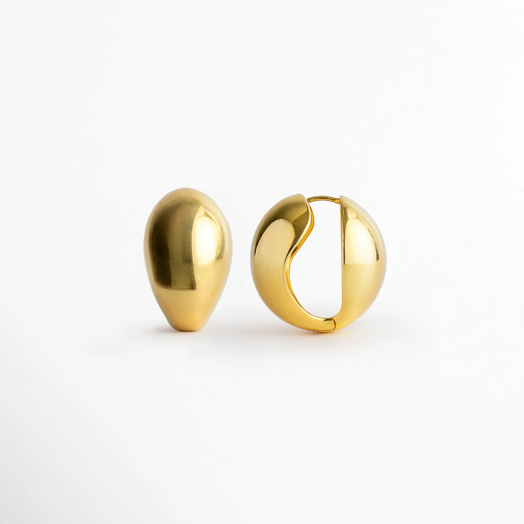 Arete Golden Nevara de perfil con la bisagra ligeramente abierta mostrando el poste integrado, Vista lateral del sistema de cierre snap/huggie de la arracada abombada en forma de gota,  Acercamiento al mecanismo de apertura en bisagra de los aretes dorados de volumen francés, Detalle del poste curvo y el encaje de seguridad de la arracada en forma de gota enchapada en oro.