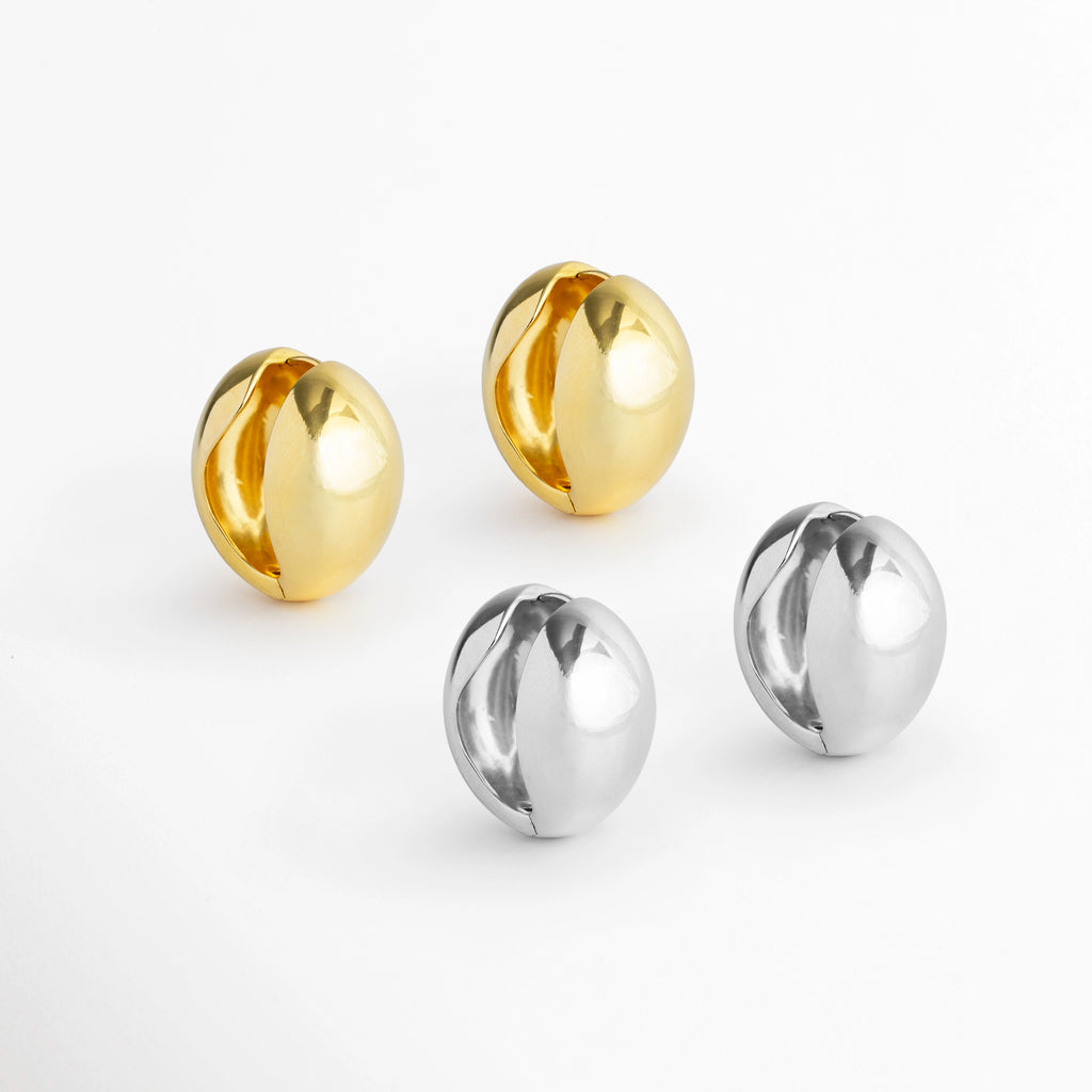 Muestra de los Aretes Nevara en sus dos variantes: par enchapado en oro brillante y par enchapado en tono plata, Vista en conjunto de los aretes en forma de gota abombada en acabados dorado y plateado sobre fondo blanco, Comparativa de estilo de los aretes esculturales tipo lágrima en tonos cálido y frío, Tomas en ángulo de los aretes de volumen francés Nevara en versiones Gold y Silver.