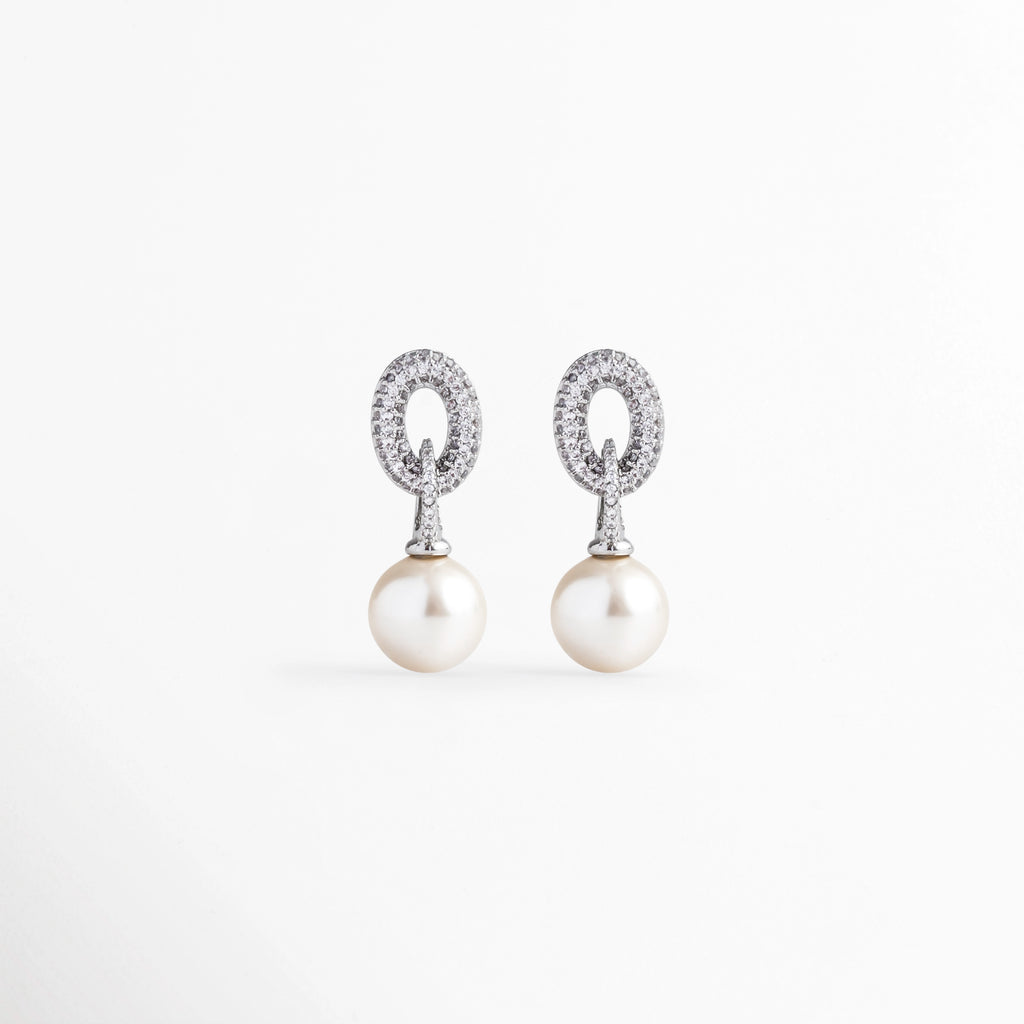 Aretes colgantes con perla sintética esférica y eslabón ovalado superior cuajado de circonias brillantes en acabado plateado, vista frontal sobre fondo blanco, Vista de frente de aretes elegantes de 2.7 cm con aro ovalado de pavé de circonias y perla blanca colgante de 1 cm, Par de aretes de novia o gala con eslabón ovalado engastado en pedrería fina y perla sintética brillante, Aretes plateados estilo drop de perla sintética y aro superior con micro pavé de circonias 
