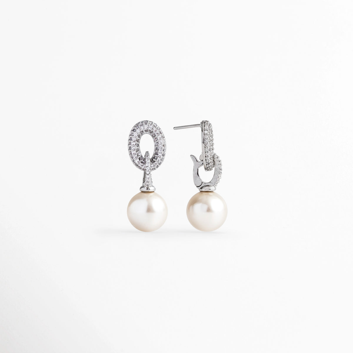 Vista de perfil de los aretes de perla mostrando el poste recto de ajuste para oreja perforada, Detalle del reverso pulido y sistema de sujeción de poste en el eslabón de circonias de los aretes, Acercamiento lateral a la montura plateada enchapada y el acabado nacarado de la perla de 1 cm, Muestra de perfil de la estructura ligera de 2.7 cm de longitud con cierre seguro.
