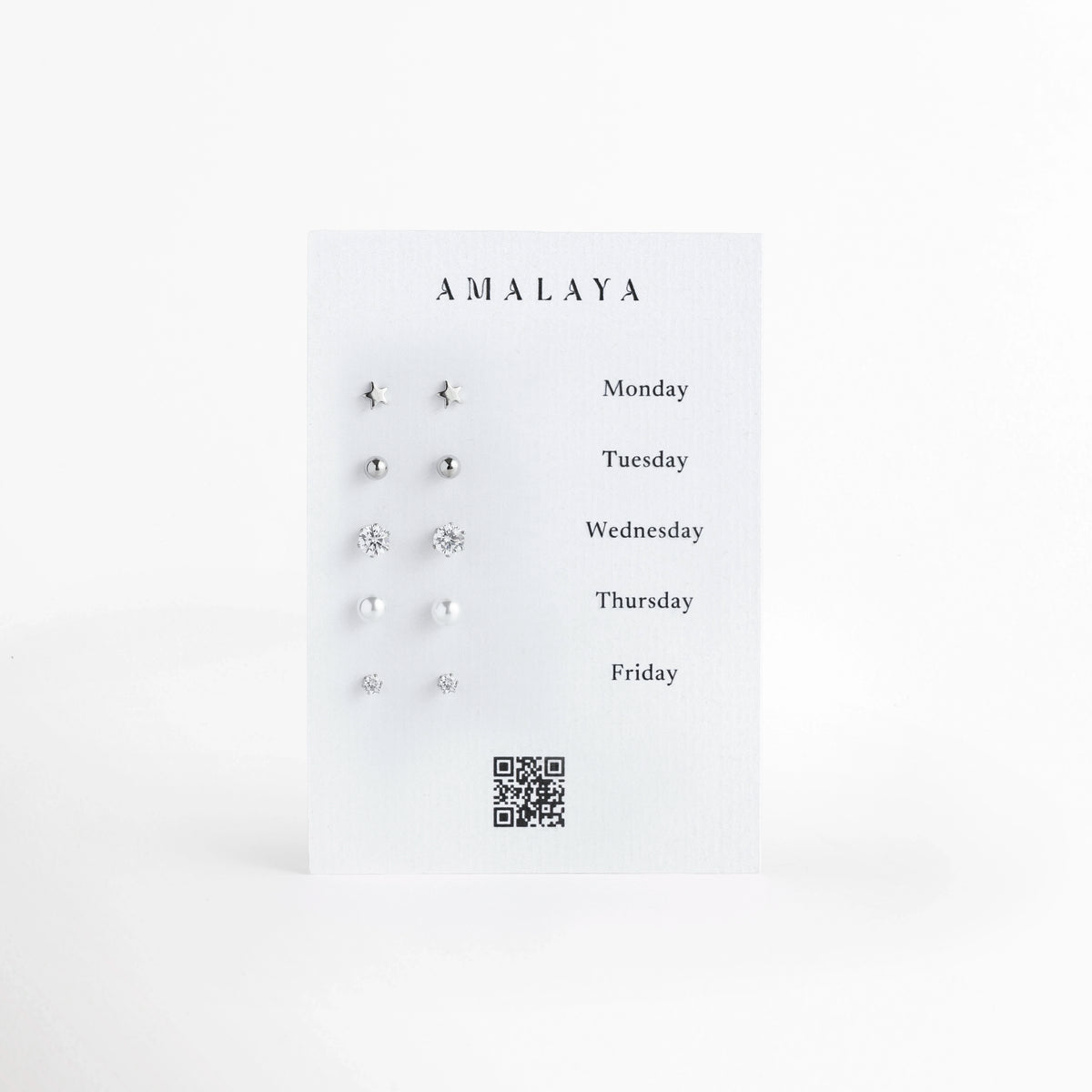 Set Silver Daily de Amalaya compuesto por cinco pares de aretes broquel enchapados en oro blanco con estrellas, esferas pulidas, circonias y perlas en tarjeta de lunes a viernes, vista frontal sobre fondo blanco,  Vista de frente del juego semanal de 5 pares de aretes stud plateados, incluyendo estrellas de 0.5 cm, esferas pulidas de 0.4 cm, circonias solitarias de 0.5 cm y 0.3 cm, y perlas nacaradas de 0.5 cm, Plano general de set de broqueles en acabado de oro blanco de estilo