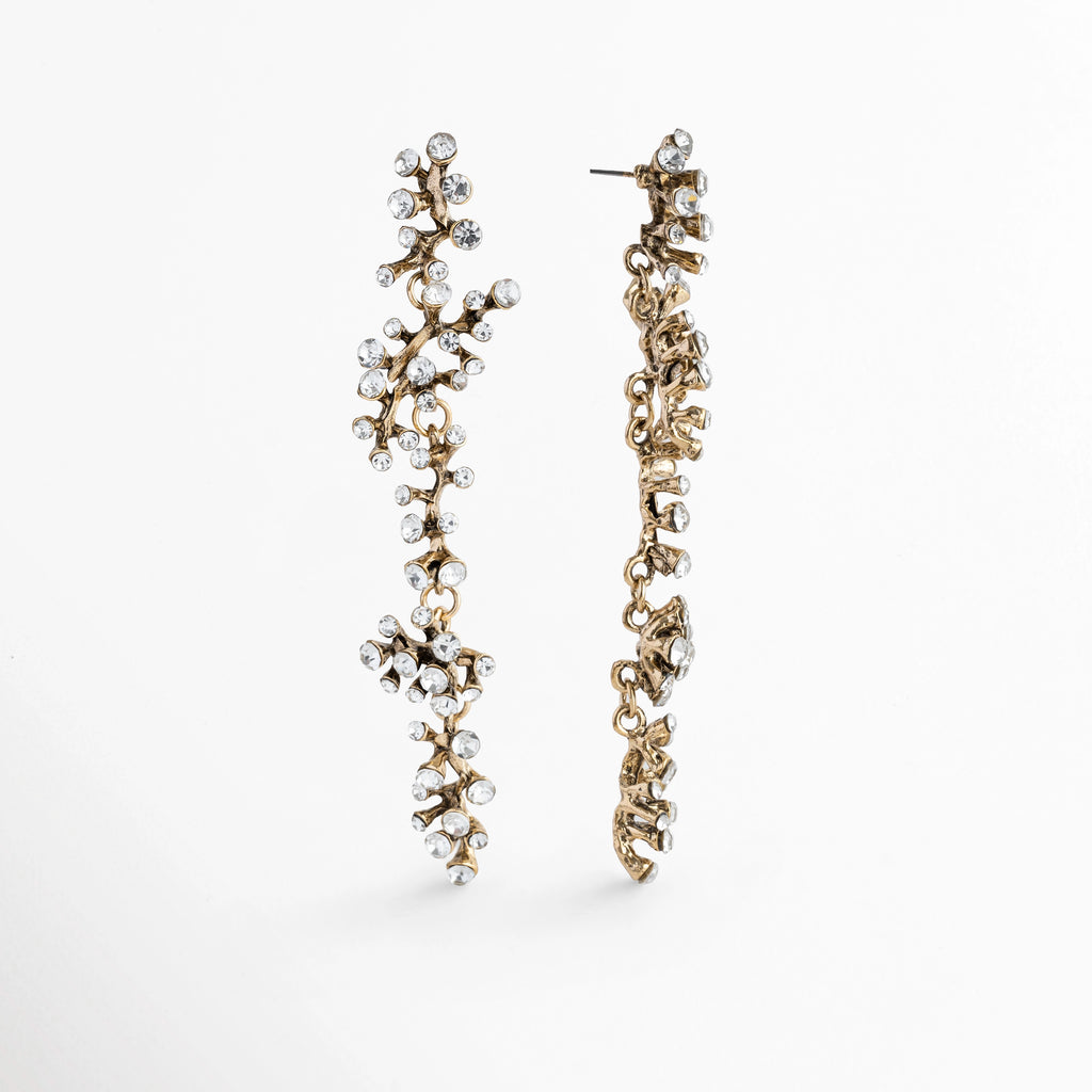 Vista de perfil de los Aretes Laurel evidenciando el poste superior de ajuste y la articulación fluida de la tira de ramas, Detalle del reverso y perfil delgado de los aretes esculturales de 9.5 cm en acero inoxidable, Acercamiento al sistema de broche de poste para oreja perforada y al trabajo de engaste posterior de las circonias, Vista lateral de los aretes alargados estilo laurel mostrando el acabado pulido brillante de la estructura.