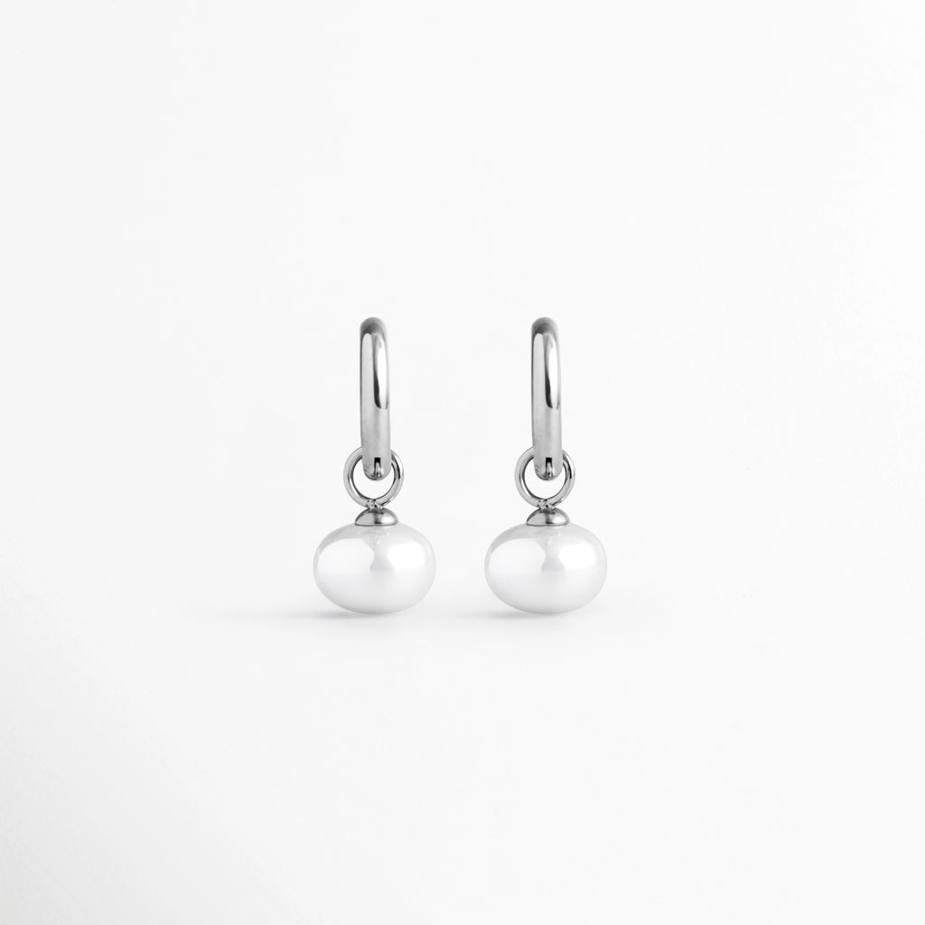 Arracadas Dune Silver Hoops enchapadas en oro blanco 16K con perla sintética colgante en forma de lágrima, vista de frente sobre fondo blanco, Vista frontal de aretes plateados tipo huggie de 3 cm de longitud con dije colgante de perla barroca sintética, Plano general de par de arracadas de acero inoxidable plateadas con perlas sintéticas nacaradas, Dune Silver Hoops enchapadas en oro blanco 16K destacando la elegancia orgánica de las perlas blancas colgantes de 1.3 cm