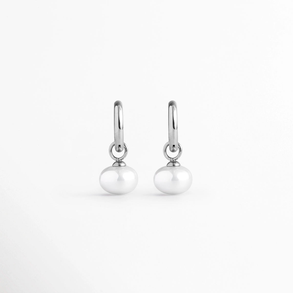 Arracadas Dune Silver Hoops enchapadas en oro blanco 16K con perla sintética colgante en forma de lágrima, vista de frente sobre fondo blanco, Vista frontal de aretes plateados tipo huggie de 3 cm de longitud con dije colgante de perla barroca sintética, Plano general de par de arracadas de acero inoxidable plateadas con perlas sintéticas nacaradas, Dune Silver Hoops enchapadas en oro blanco 16K destacando la elegancia orgánica de las perlas blancas colgantes de 1.3 cm