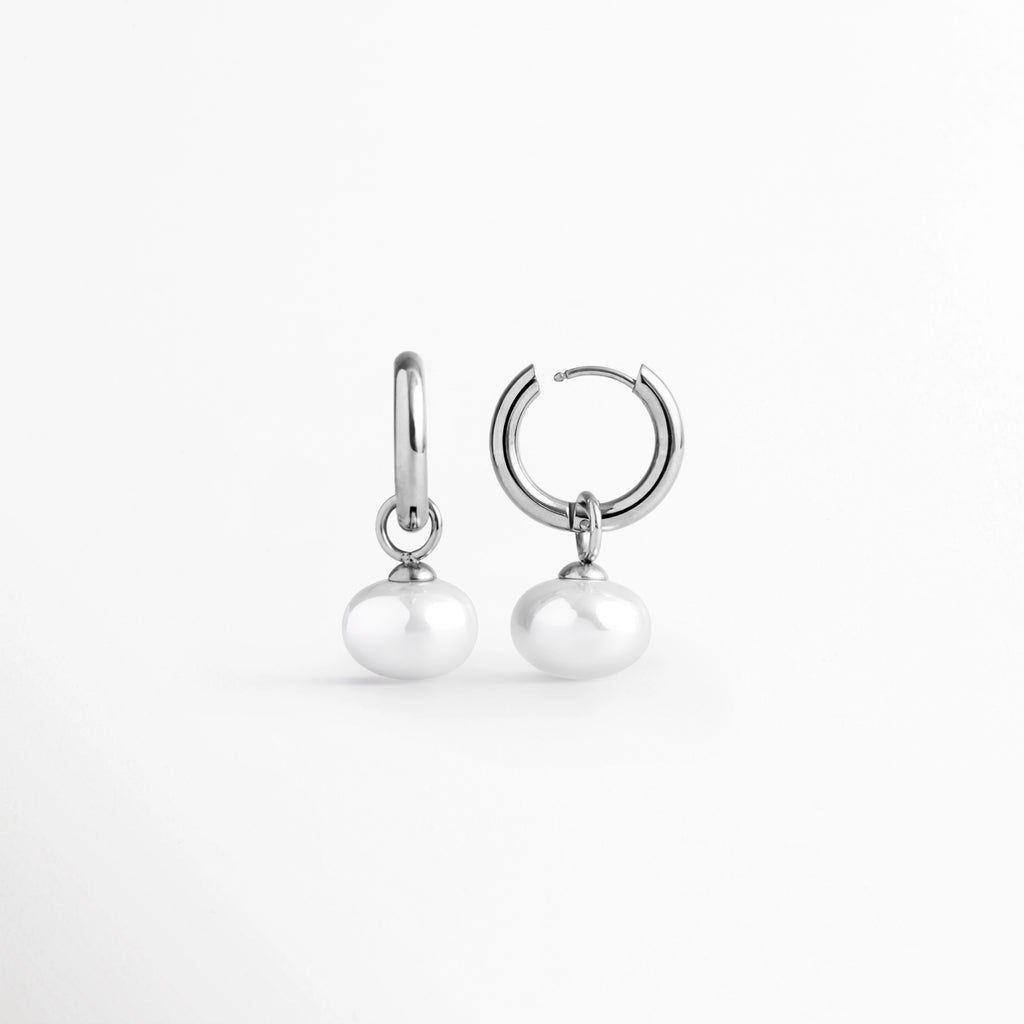 Acercamiento al sistema de cierre de bisagra tipo huggie abierto de la arracada Dune Silver Hoop, Vista macro del mecanismo de broche a presión y el reverso texturizado del aro plateado enchapado en oro blanco 16K, Detalle de la articulación de la arracada en acero inoxidable y la argolla de sujeción de la perla sintética, Muestra de la apertura del broche tipo clic que facilita la colocación cómoda y segura del arete plateado.
