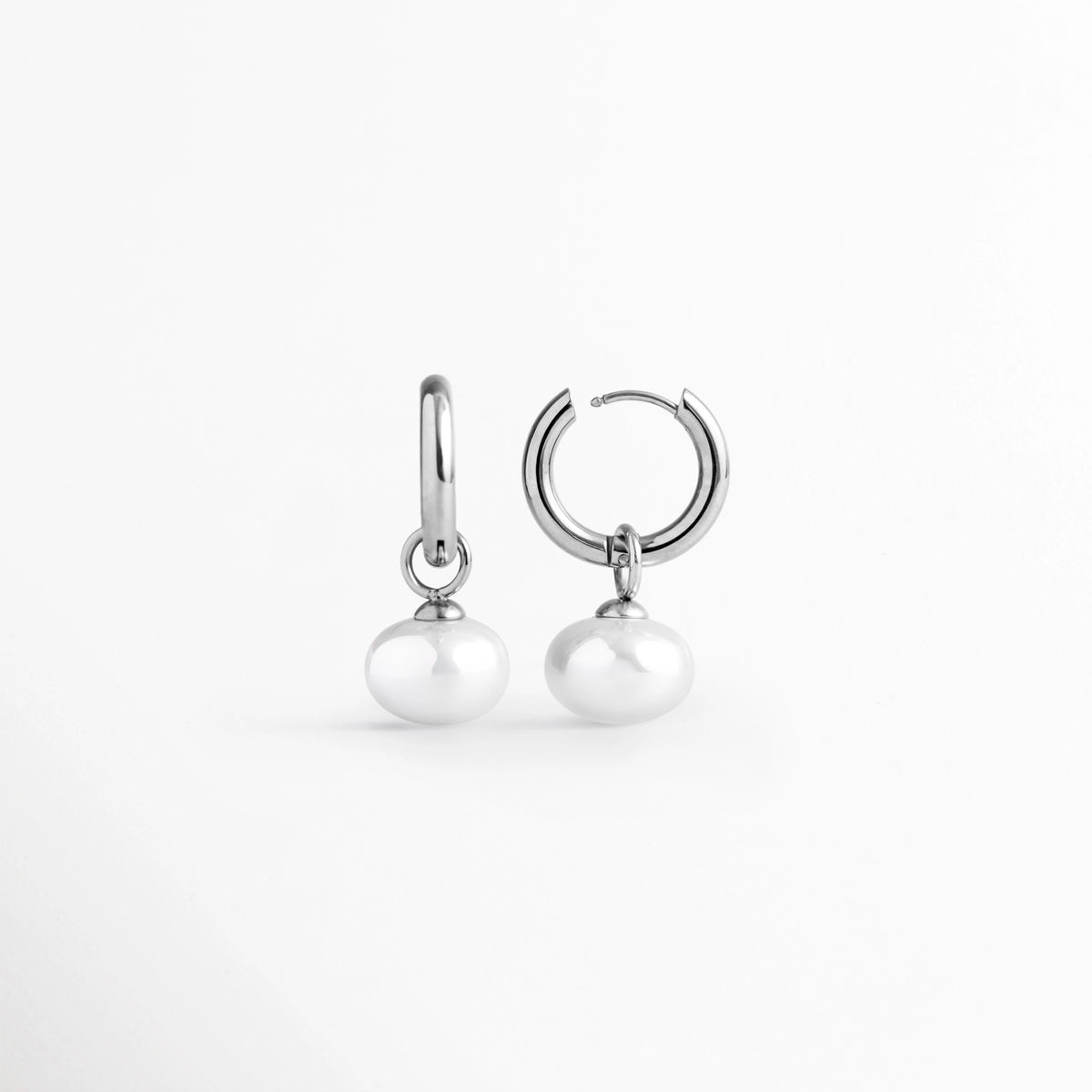 Acercamiento al sistema de cierre de bisagra tipo huggie abierto de la arracada Dune Silver Hoop, Vista macro del mecanismo de broche a presión y el reverso texturizado del aro plateado enchapado en oro blanco 16K, Detalle de la articulación de la arracada en acero inoxidable y la argolla de sujeción de la perla sintética, Muestra de la apertura del broche tipo clic que facilita la colocación cómoda y segura del arete plateado.