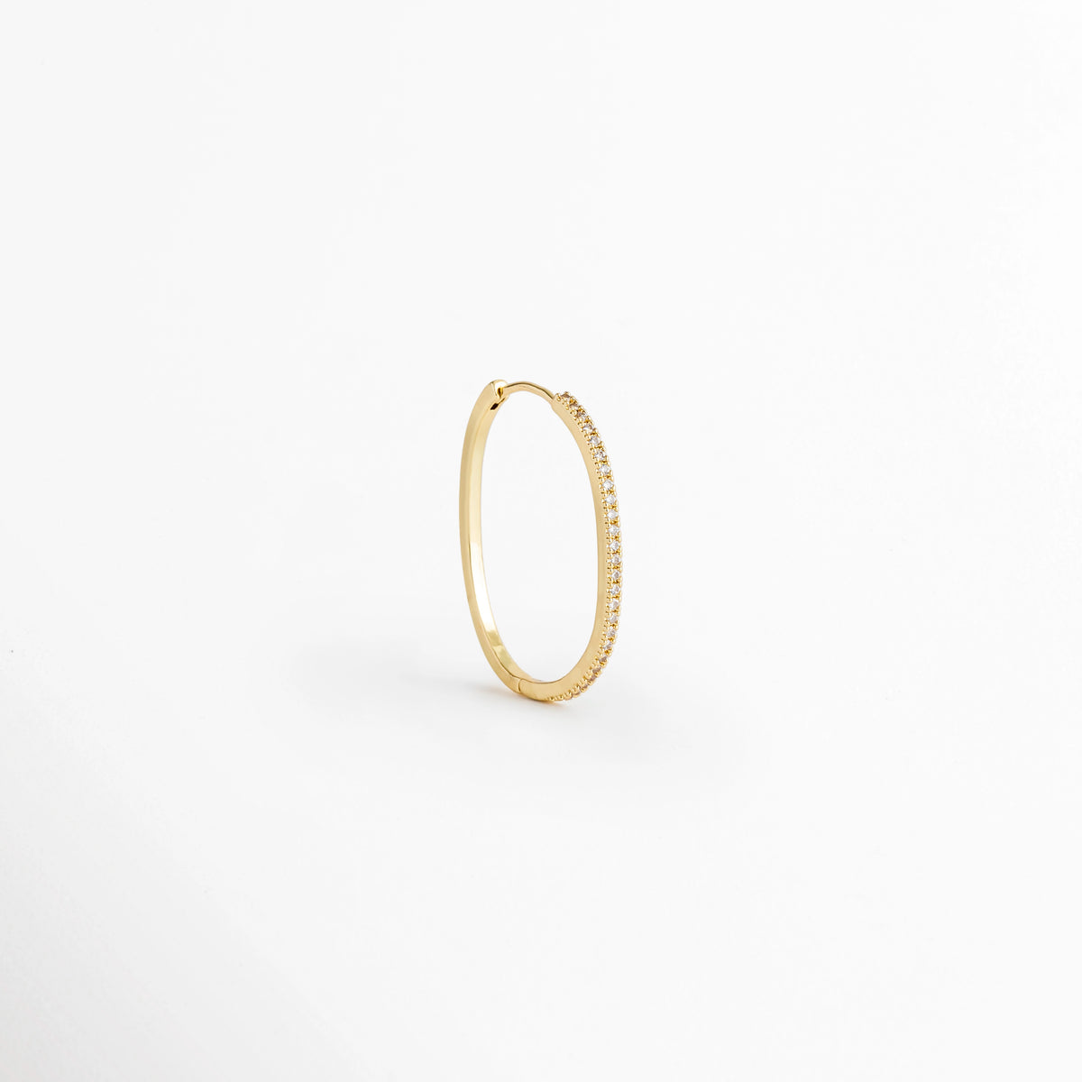 Arracada individual del Set Golden Hoops vista en perspectiva de perfil mostrando la delgada silueta dorada y el cierre continuo, Vista lateral de una arracada fina de cobre enchapada en oro 14K con perfil estilizado, Arracada de aro delgado dorada vista en ángulo de tres cuartos sobre fondo claro,  Detalle de curvatura y grosor fino de arracada con pavé de circonia incrustada.