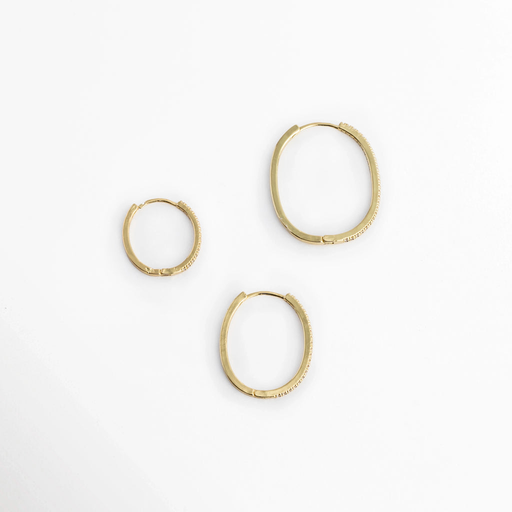 Muestra de los tres tamaños individuales de arracadas (2.1 cm, 2.9 cm y 3.2 cm) distribuidos sobre superficie blanca, Comparación de escala de los tres aros delgados dorados con pavé de circonias transparentes, Vista superior de tres arracadas enchapadas en oro 14K ordenadas por dimensión de menor a mayor, Trío de aros estilo huggie y arracada media con incrustaciones de circonias cristalinas.