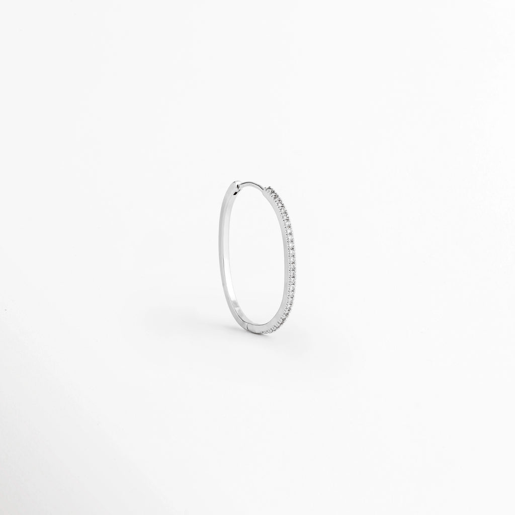 Arracada individual del Set Silver Hoops vista en perspectiva de perfil mostrando la delgada silueta plateada y el cierre continuo, Vista lateral de una arracada fina de cobre con baño plateado de perfil estilizado, Arracada de aro delgado plateada vista en ángulo de tres cuartos sobre fondo claro, Detalle de curvatura y grosor fino de arracada plateada con pavé de circonia incrustada.