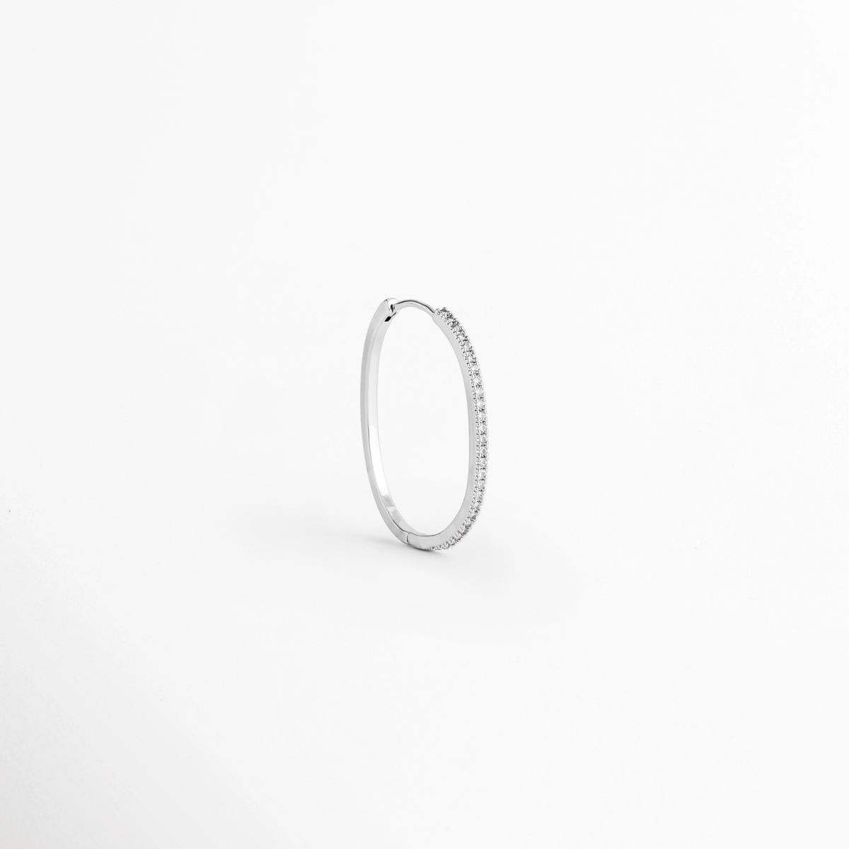 Arracada individual del Set Silver Hoops vista en perspectiva de perfil mostrando la delgada silueta plateada y el cierre continuo, Vista lateral de una arracada fina de cobre con baño plateado de perfil estilizado, Arracada de aro delgado plateada vista en ángulo de tres cuartos sobre fondo claro, Detalle de curvatura y grosor fino de arracada plateada con pavé de circonia incrustada.