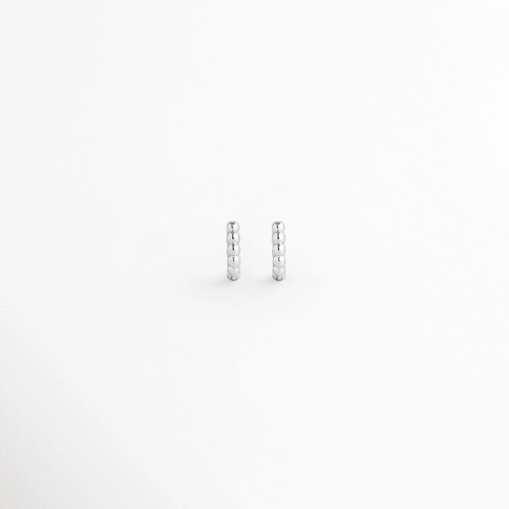 Arracada Silver de 8 mm con textura de cuentas esféricas alineadas en tono plata brillante, vista frontal de par sobre fondo blanco, Vista de frente de pequeñas arracadas plateadas tipo huggie de 0.8 cm de diámetro con relieve perlado, Par de aros diminutos de 8 mm en electrochapado plateado con textura de esferas continuas y alto brillo, Arracadas plateadas de 8 mm con textura de bolitas para segundo o tercer orificio sobre fondo claro