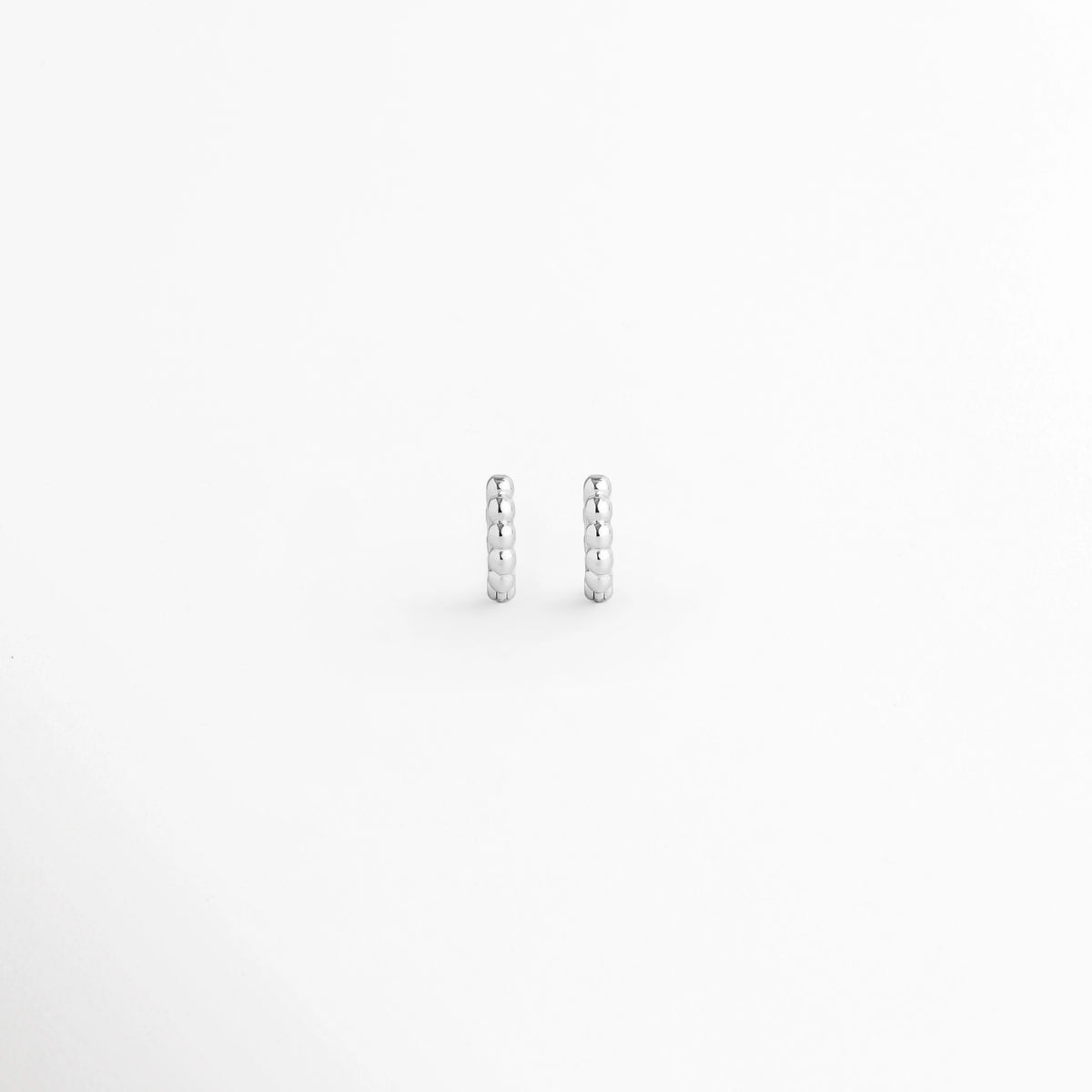 Arracada Silver de 8 mm con textura de cuentas esféricas alineadas en tono plata brillante, vista frontal de par sobre fondo blanco, Vista de frente de pequeñas arracadas plateadas tipo huggie de 0.8 cm de diámetro con relieve perlado, Par de aros diminutos de 8 mm en electrochapado plateado con textura de esferas continuas y alto brillo, Arracadas plateadas de 8 mm con textura de bolitas para segundo o tercer orificio sobre fondo claro