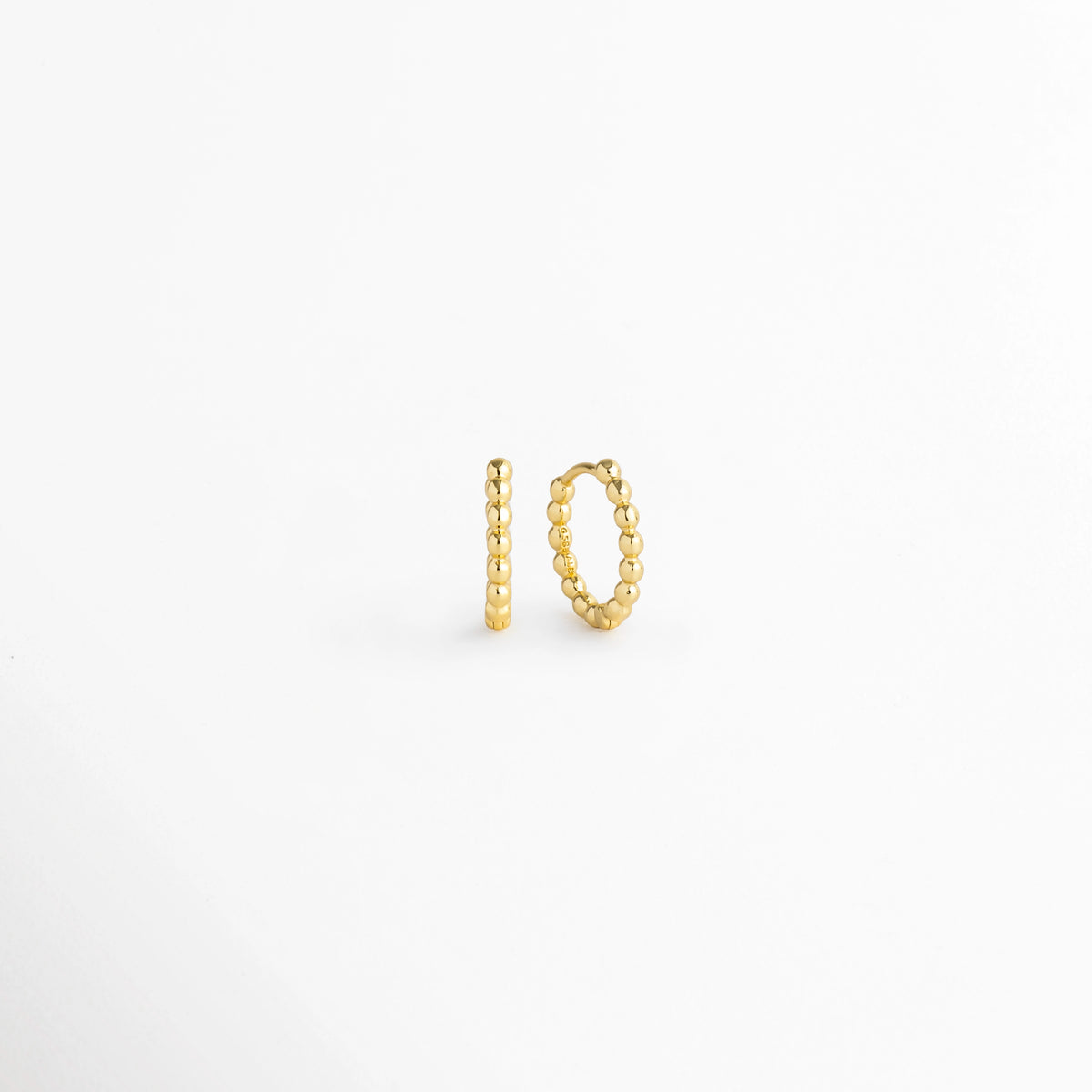 Arracadas Golden Hoops vistas de perfil y tres cuartos mostrando la silueta circular perlada y la Bisagra de apertura, Vista en ángulo de aretes tipo huggie dorados resaltando la textura de cuentas redondeadas de su superficie, Acercamiento a la silueta circular con textura de bolitas doradas en toma de tres cuartos sobre fondo claro, Detalle del diámetro compacto de la arracada perlada Golden Hoops enchapada en oro.