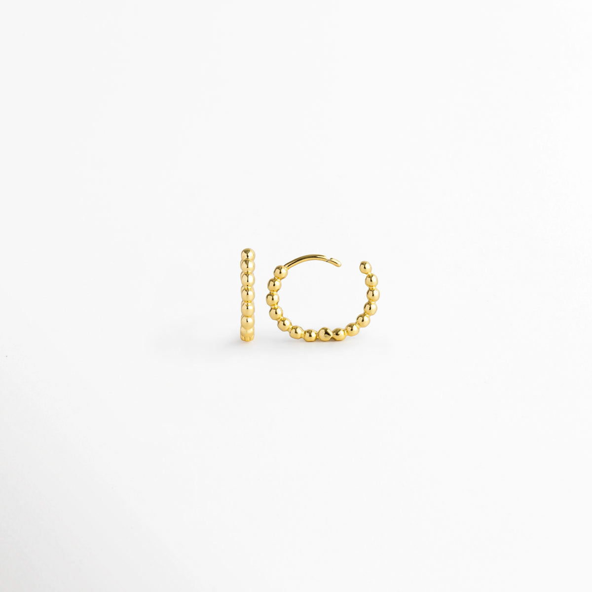 Vista lateral de la arracada Golden Hoops con la bisagra completamente abierta mostrando el poste de inserción, Acercamiento al broche articulado abierto de la arracada dorada con textura de bolitas continuas, Detalle del sistema de apertura fácil de la arracada estilo huggie sobre fondo claro.