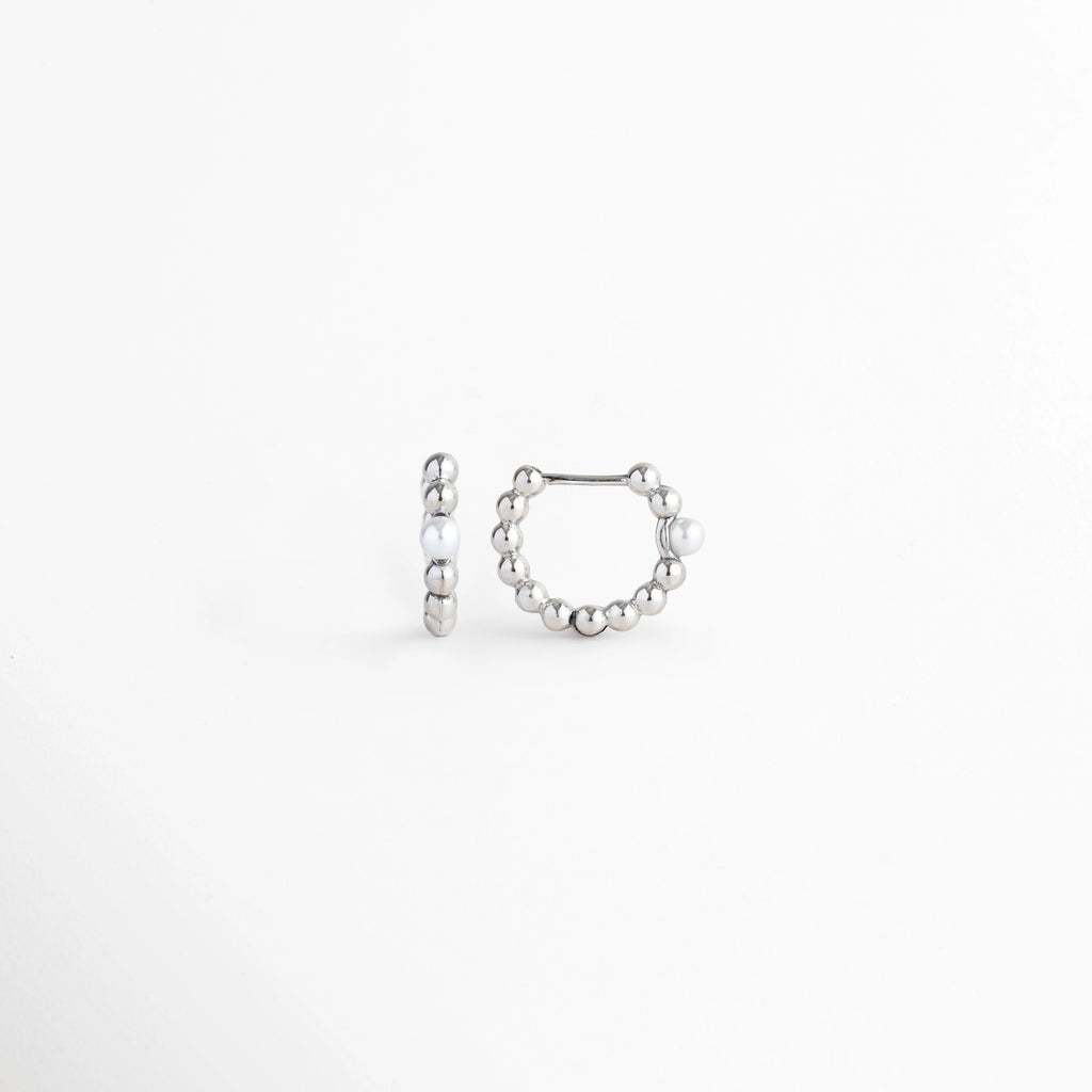 Vista lateral de los Silver Pearl Hoops exhibiendo el perfil circular compacto y el mecanismo de cierre a presión, Acercamiento de lado a la curvatura del aro metálico plateado con cuentas alineadas, Toma lateral que muestra el poste delgado articulado para un ajuste seguro en la oreja, Muestra del acabado electrochapado en tono plata pulido y la simetría del aro.