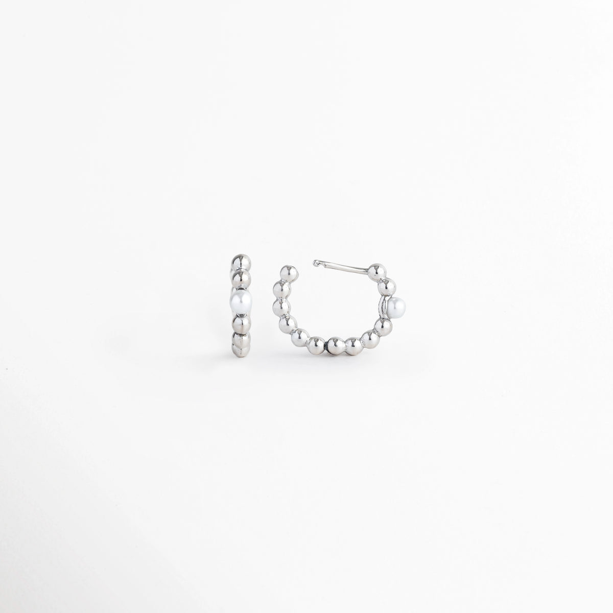 Vista de los Silver Pearl Hoops en ángulo con el poste articulado extendido preparado para colocación, Acercamiento al sistema de clic o bisagra invisible en la base de las arracadas plateadas, Detalle de la superficie metálica pulida y la perla blanca de acento sobre fondo blanco, Muestra de la solidez y practicidad del cierre abrazadera (huggie)