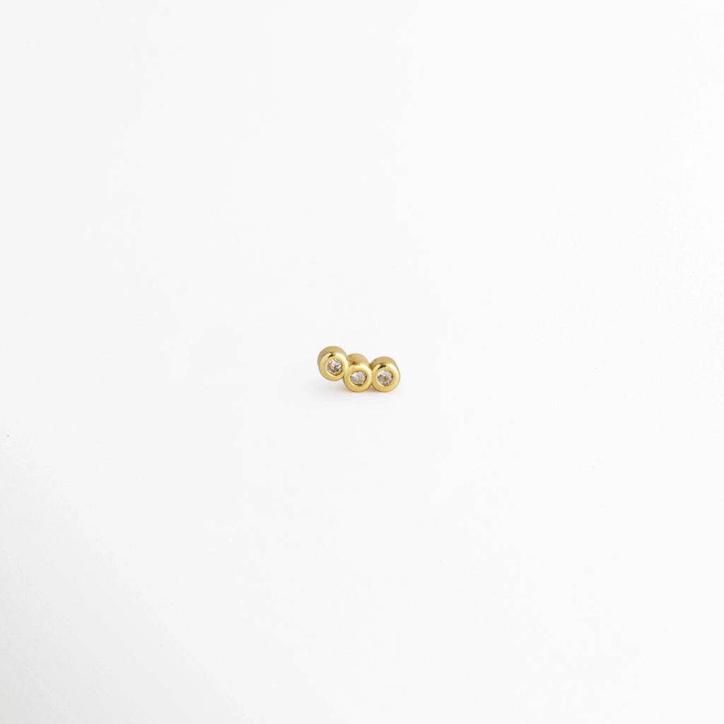 Piercing Laguna enchapado en oro 18K con diseño curvado de tres circonias transparentes alineadas en bisel, vista frontal sobre fondo blanco, Piercing para hélix o tragus de cobre enchapado en oro 18K con racimo curvado de tres gemas cristalinas, Vista de frente de piercing labret o barbell con tres circonias en arcada sobre superficie clara, Piercing dorado pequeño con trío de circonias en línea curva de diseño delicado sobre fondo neutro.