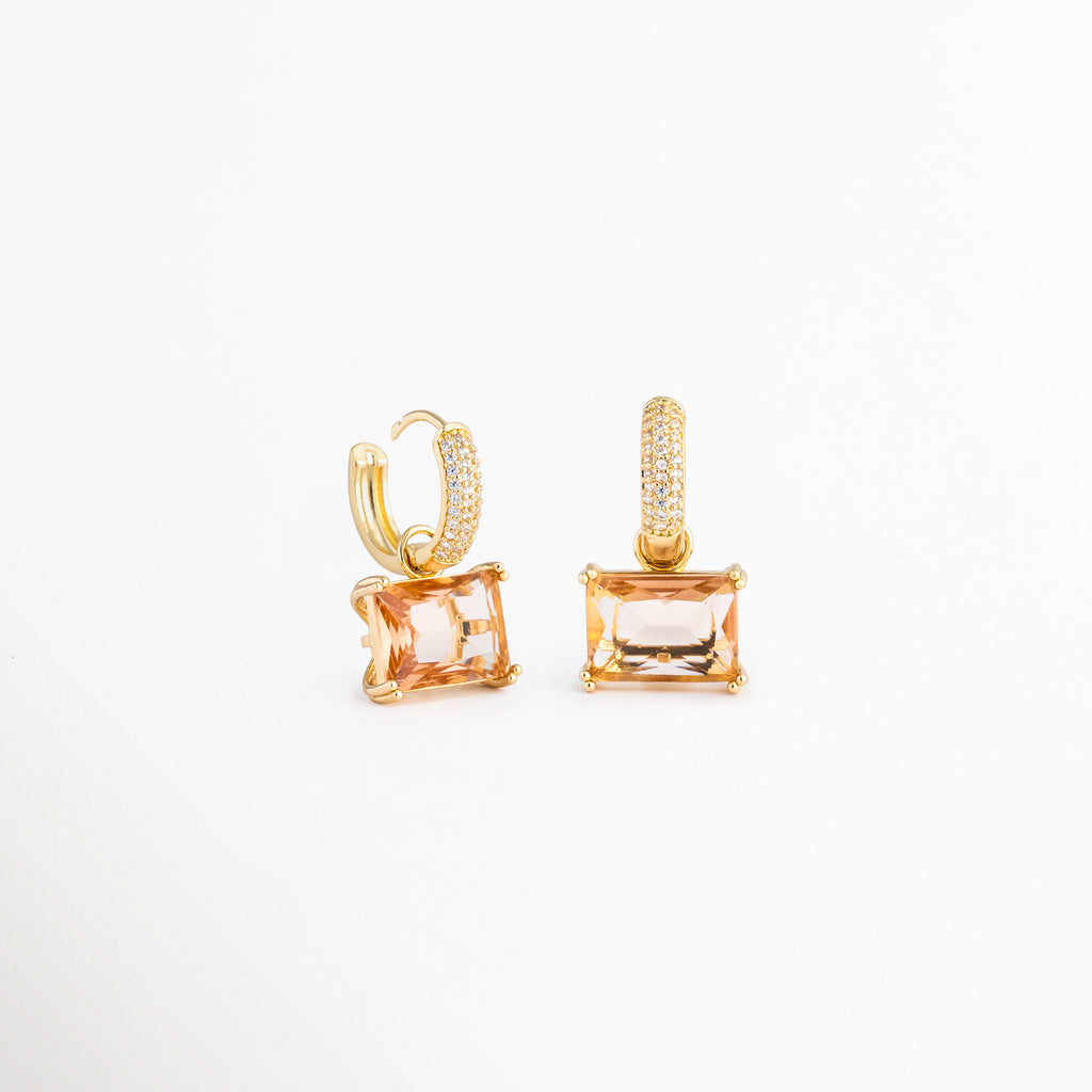 Par de aretes Soju con baño de oro de 18K y gemas rectangulares traslúcidas, Vista de catálogo de los pendientes de aro con cristales finos colgantes, Aretes de fiesta y diario con acabado dorado pulido y piedras rectangulares, Detalle de los reflejos del cristal color champaña en los aretes de chapa de oro, Perspectiva completa del set de pendientes pequeños con dije geométrico de cristal.