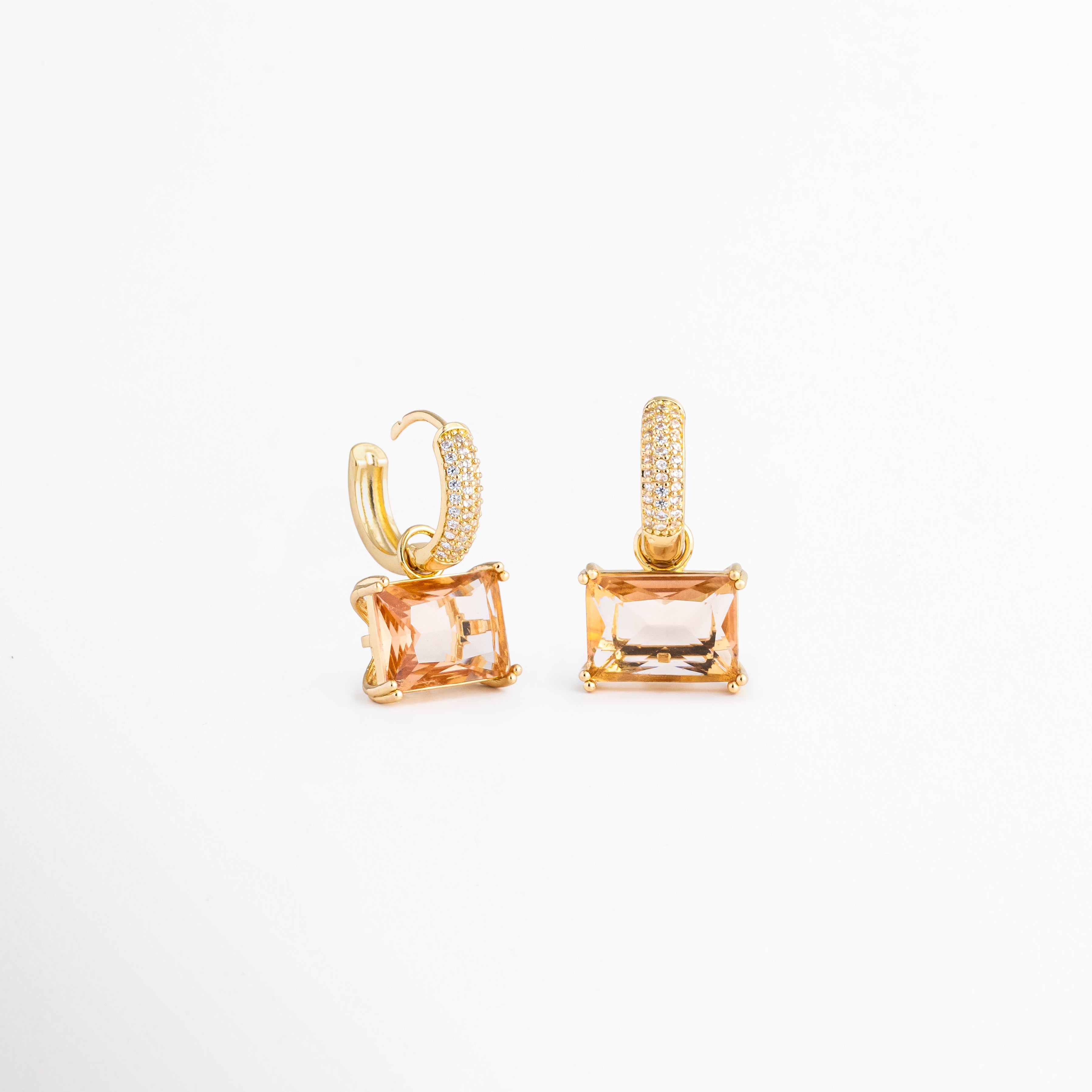 Par de aretes Soju con baño de oro de 18K y gemas rectangulares traslúcidas, Vista de catálogo de los pendientes de aro con cristales finos colgantes, Aretes de fiesta y diario con acabado dorado pulido y piedras rectangulares, Detalle de los reflejos del cristal color champaña en los aretes de chapa de oro, Perspectiva completa del set de pendientes pequeños con dije geométrico de cristal.