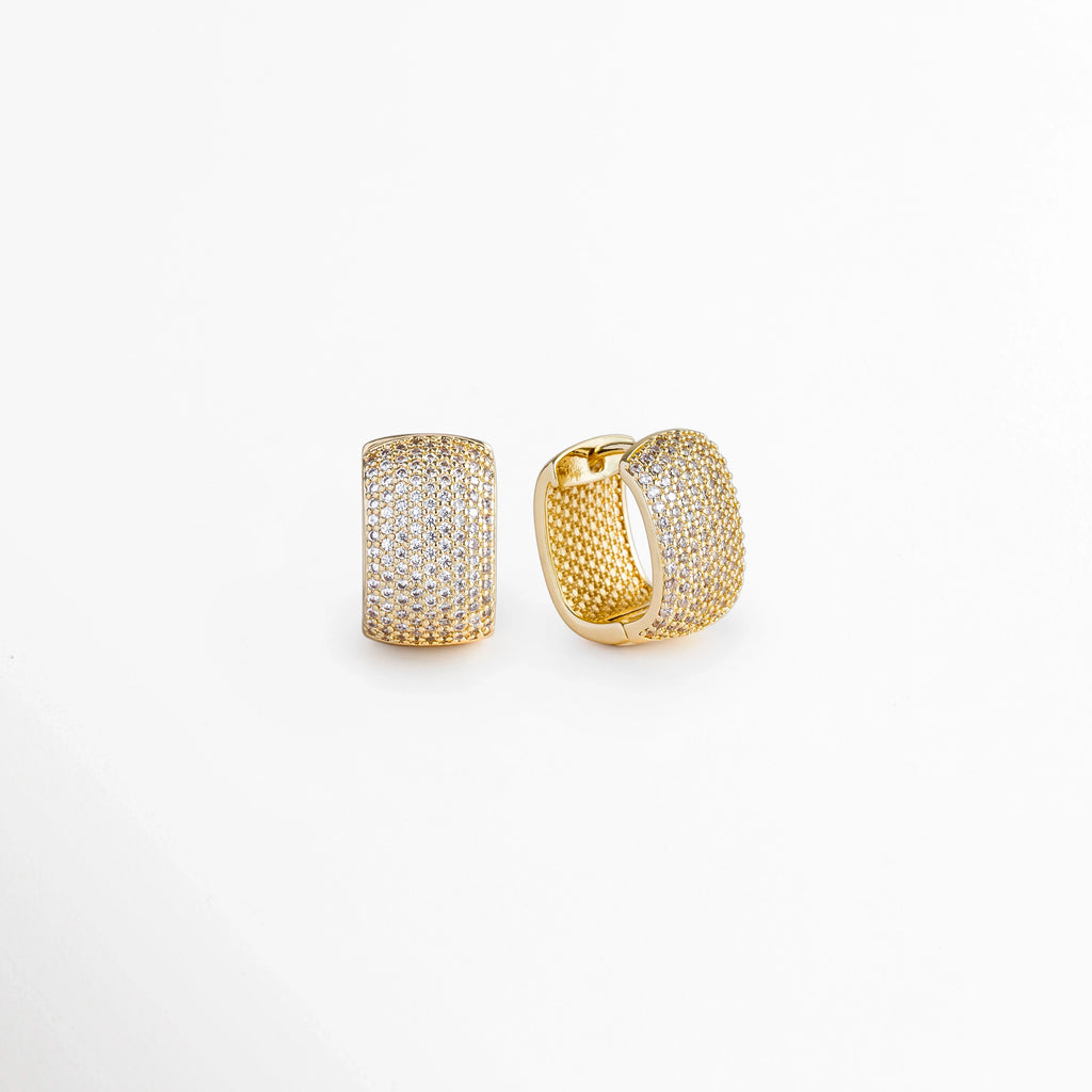 Vista en tres cuartos de los Aretes Bori Golden mostrando el volumen abombado del perfil y el cierre articulado tipo huggie, Acercamiento lateral a las arrancadas doradas anchas de 1.8 cm de longitud con incrustaciones de piedras artificiales de corte brillante, Toma en ángulo que resalta la textura de micro-pavé y la curvatura ergonómica que rodea el lóbulo, Muestra del grosor de la caña dorada y el brillo de la pedrería cristalina enchapada en oro 18K.