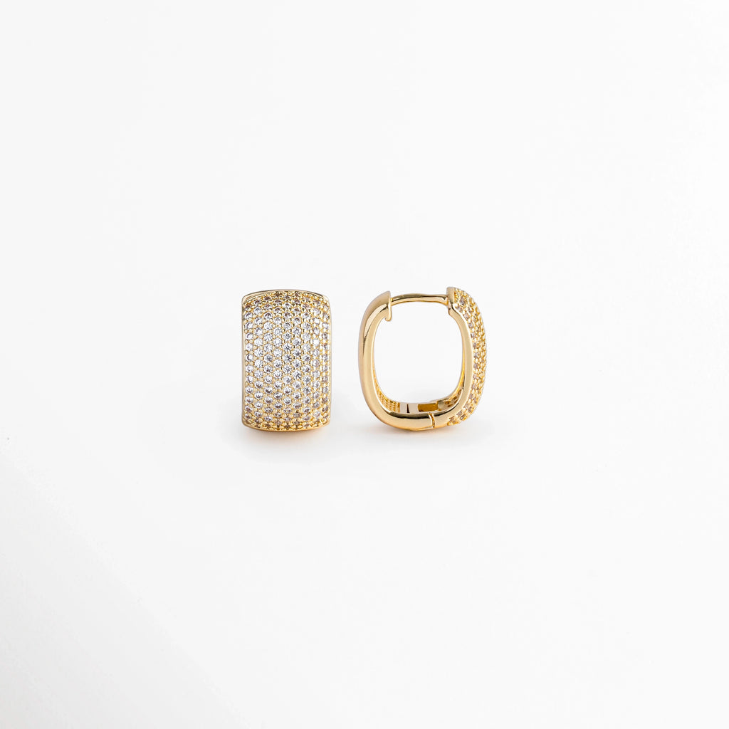Vista de perfil de uno de los Aretes Bori Golden mostrando el mecanismo de bisagra central y el poste de cierre clic, Acercamiento al sistema de sujeción abraza-lóbulo de la arrancada ancha enchapada en oro 18K, Toma lateral que muestra el reverso metálico pulido y la articulación del broche de seguridad tipo huggie, Muestra del perfil redondeado de 1.8 cm de alto con reverso dorado e incrustación frontal de piedras.  