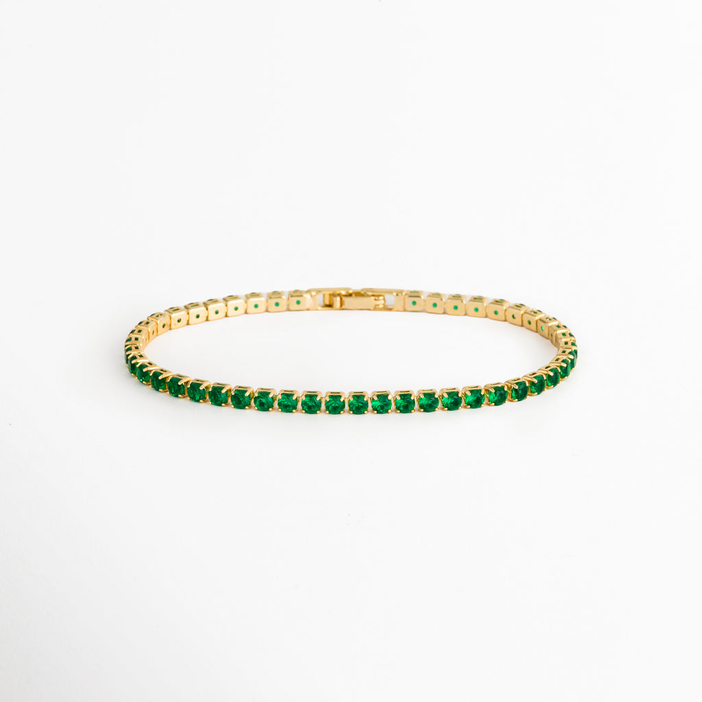 Tennis Bracelet Green Grace enchapada en oro 18K con hilera continua de circonias verde esmeralda de corte brillante, vista de frente sobre fondo blanco, Vista frontal de pulsera tennis delgada de 0.3 cm de ancho con gemas de circonia verde y engaste de garras doradas, Plano general de brazalete estilo tennis de cobre enchapado en oro 18K con pedrería verde brillante, Tennis Bracelet Green Grace mostrando la secuencia uniforme de circonias verdes de 18 cm